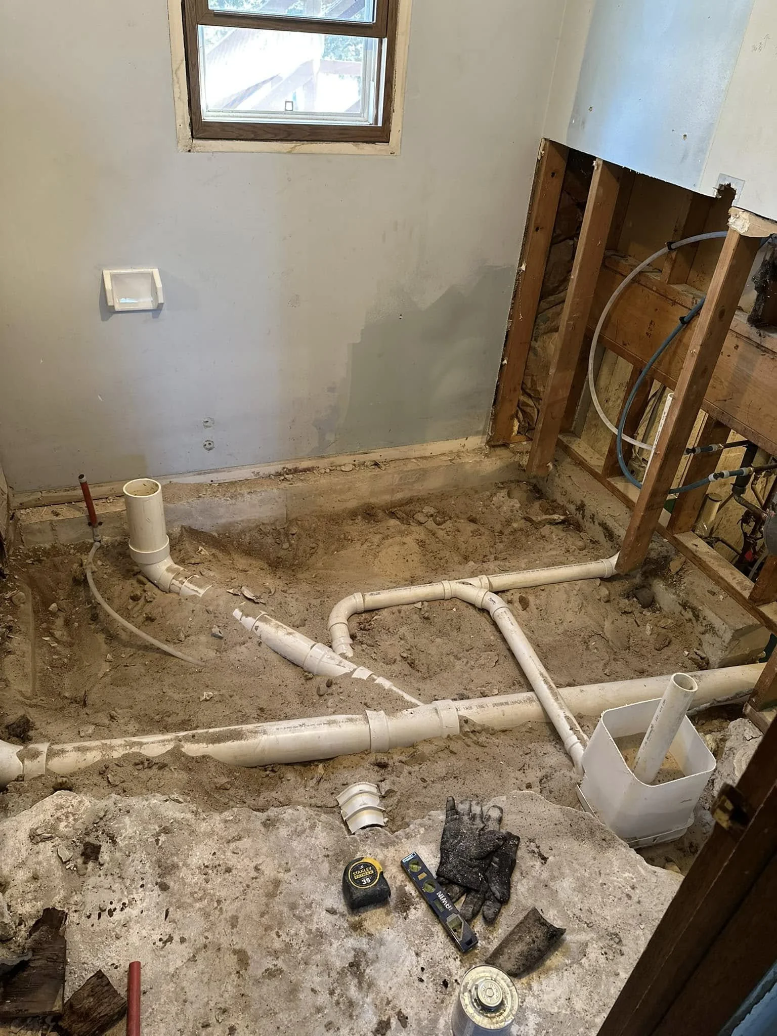 A construction site showing exposed plumbing pipes and unfinished walls in a room during renovation.