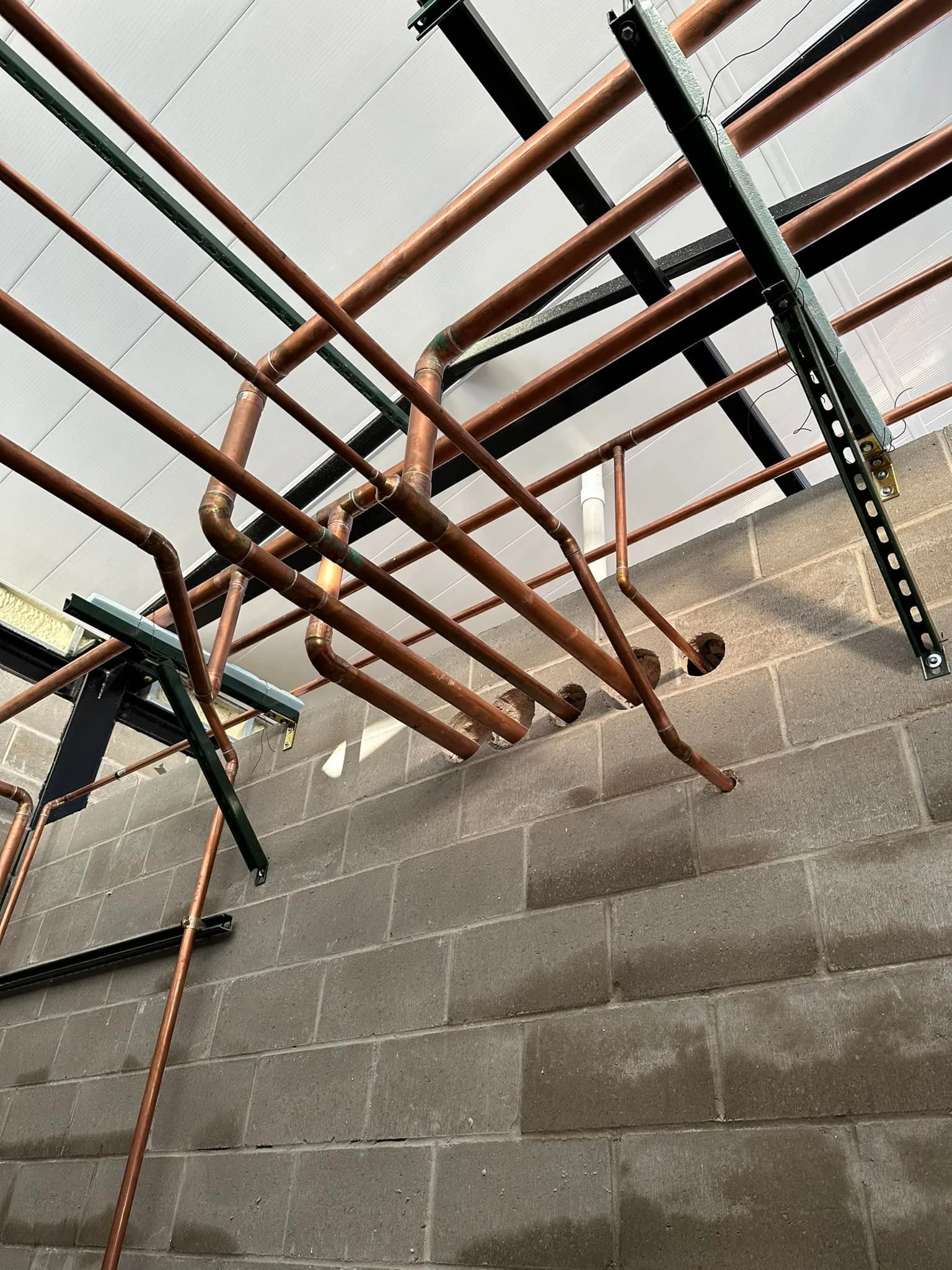 Copper pipes installed along the ceiling and wall, with black metal brackets supporting them, in a building under construction or renovation.