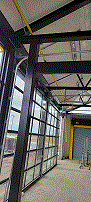 Indoor shopping mall with glass storefronts, steel beams, and a tiled floor.