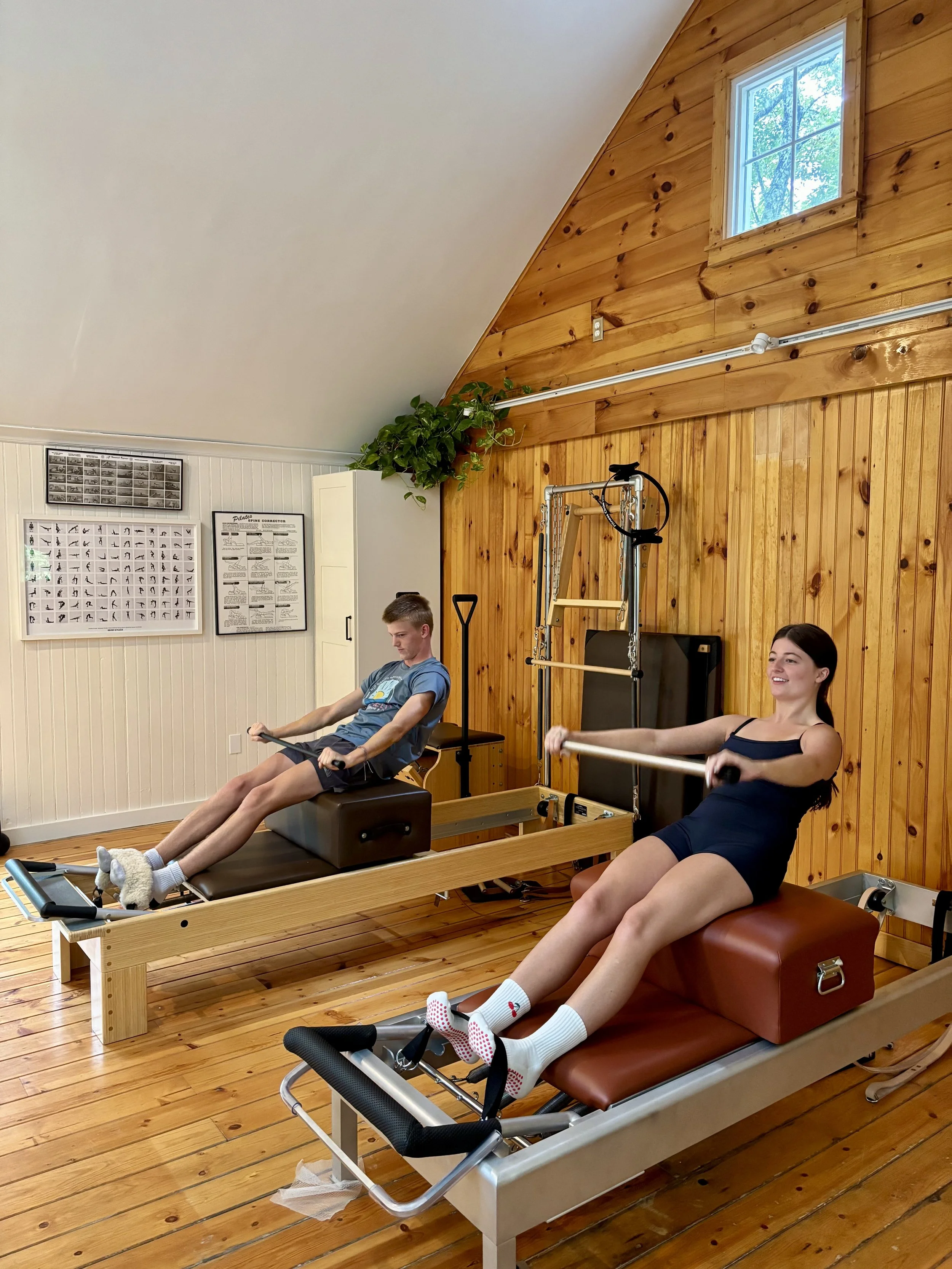 Two reformers are great to practice Pilates with a friend. Two people sitting individually on the reformer doing short box with a pole.