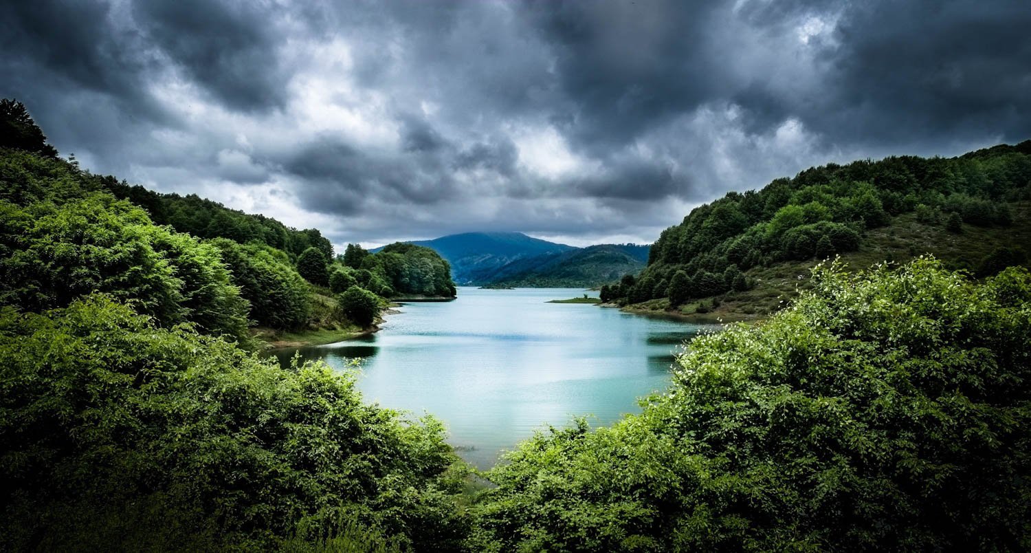 A scenic view of a river flowing between lush green hills under a cloudy sky.