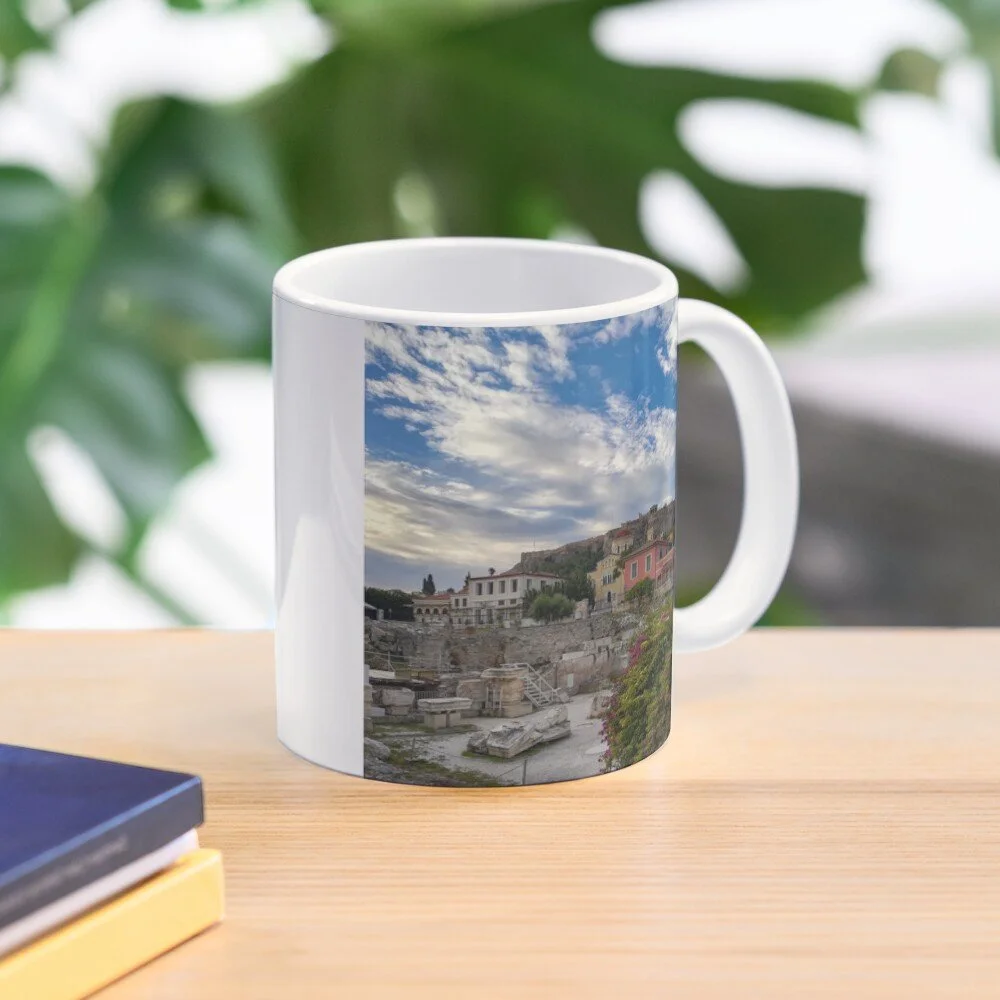 White mug with a scenic photo of ancient ruins, colorful buildings, and a cloudy sky printed on it, sitting on a wooden surface with books nearby.