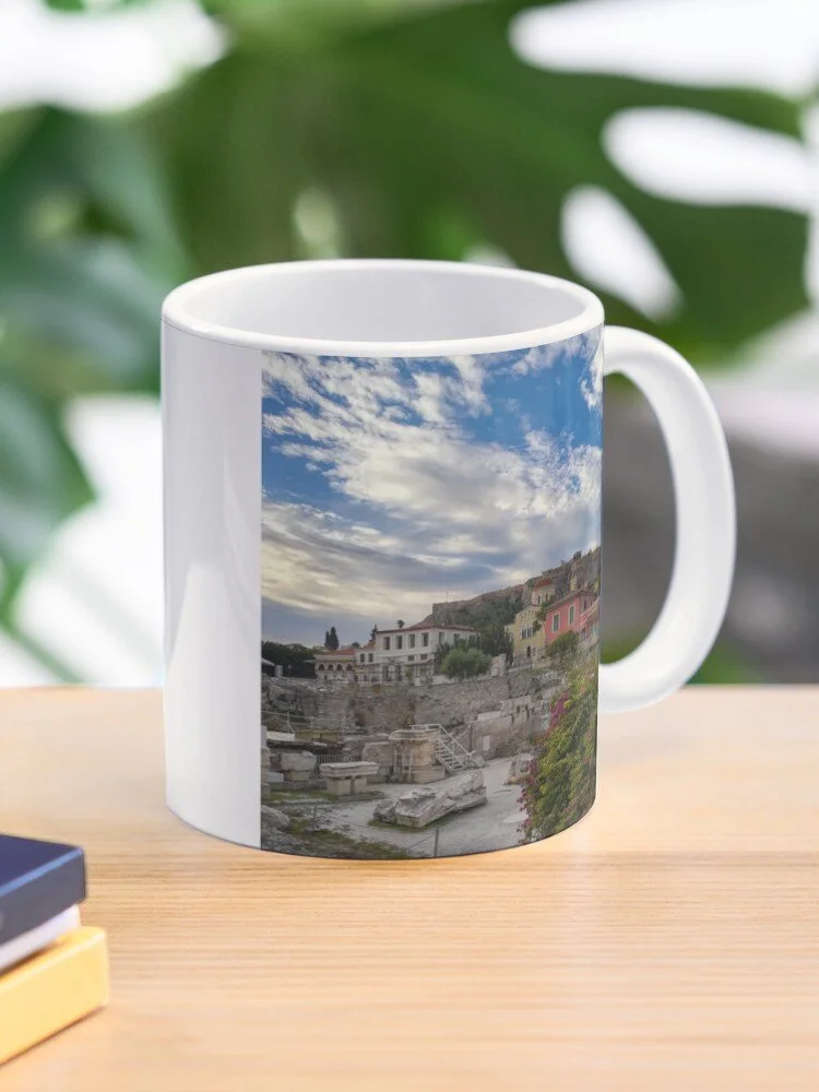 White ceramic mug with a scenic image of rocky ruins, colorful houses, and a cloudy sky, placed on a wooden table.
