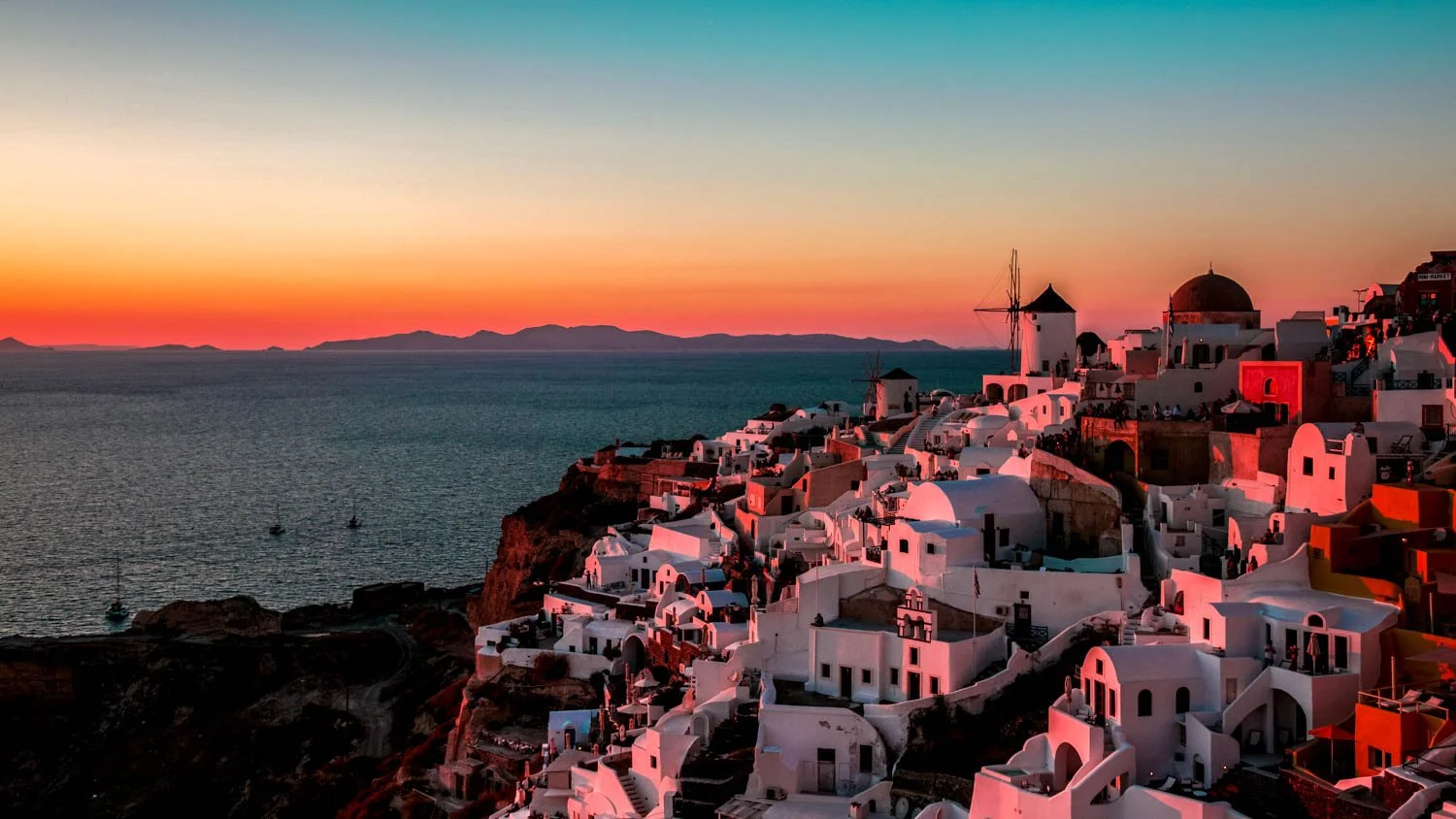 Sunset over the Greek island of Santorini with white buildings, windmills, and a colorful sky