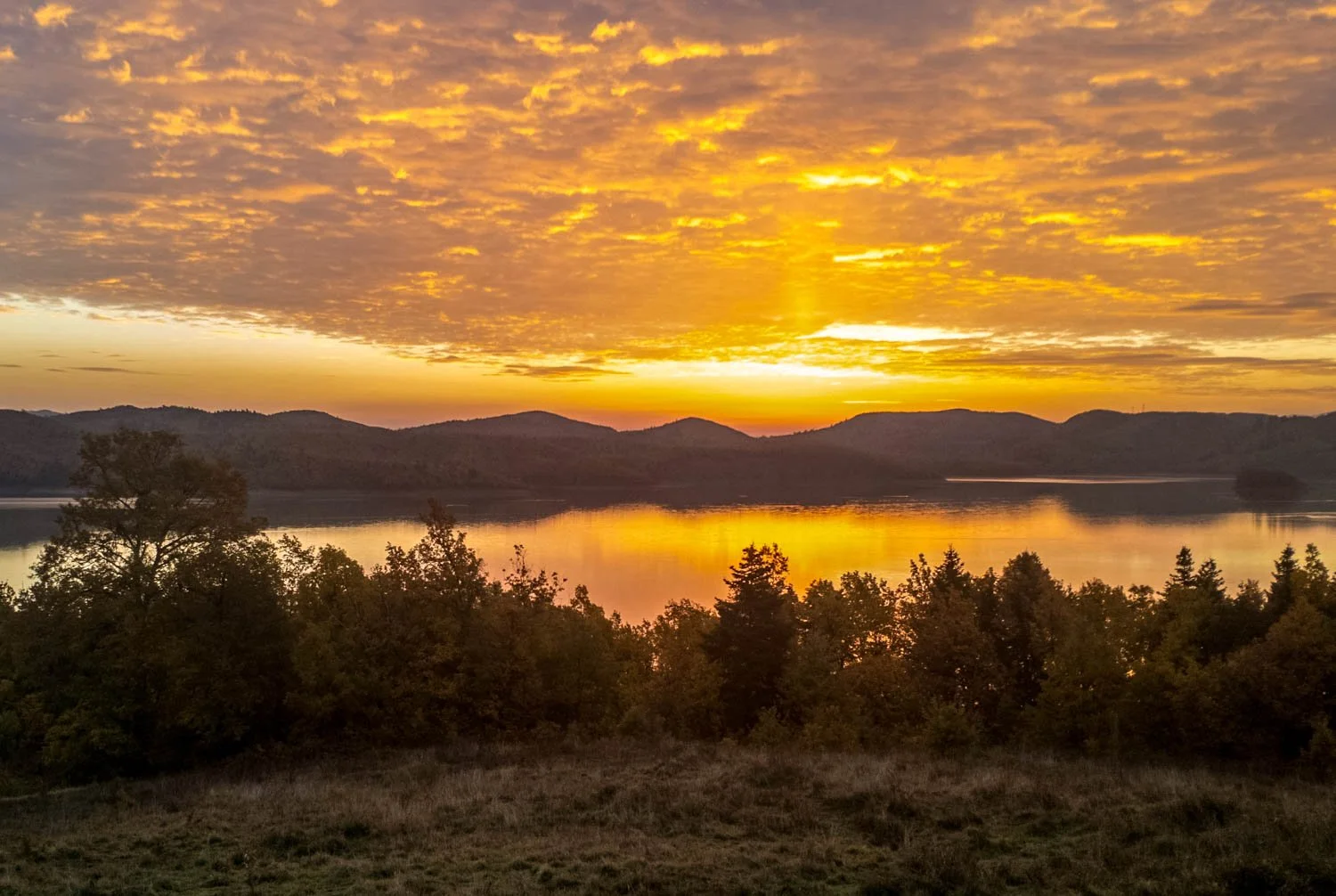 Sunset over a lake with mountains in the background and trees in the foreground.