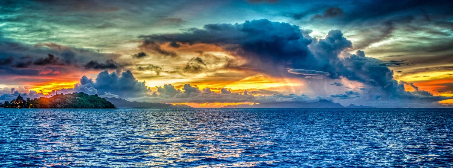 A vibrant sunset over a body of water with clouds in the sky and a distant island or landmass on the horizon.