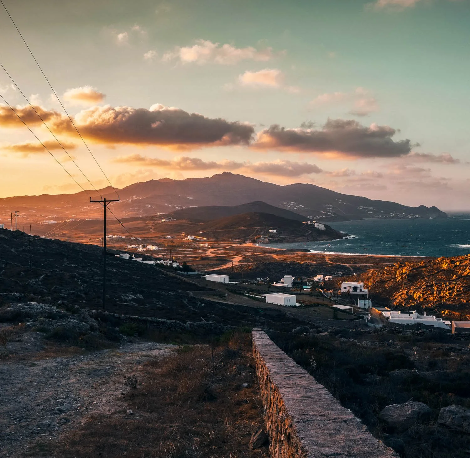 Sunset over a coastline with mountains in the background, a few clouds in the sky, and white buildings in the foreground.