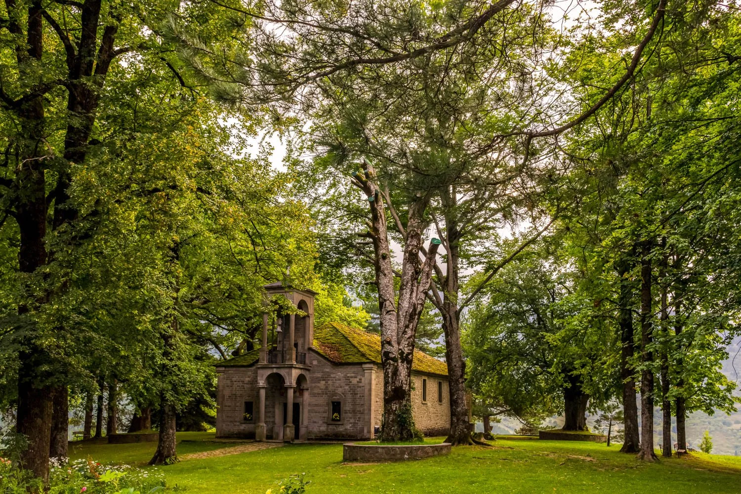 Small stone church surrounded by lush green trees and grass.