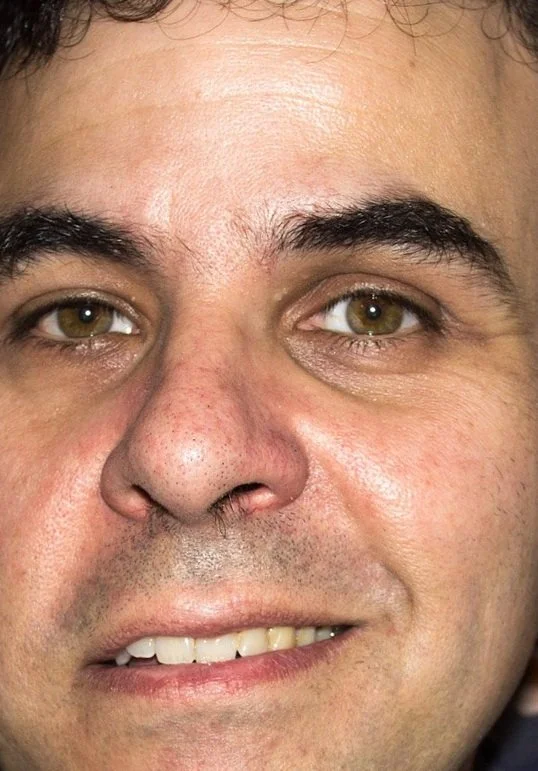 Close-up of a person's face with short dark hair, brown eyes, and slightly smiling expression.