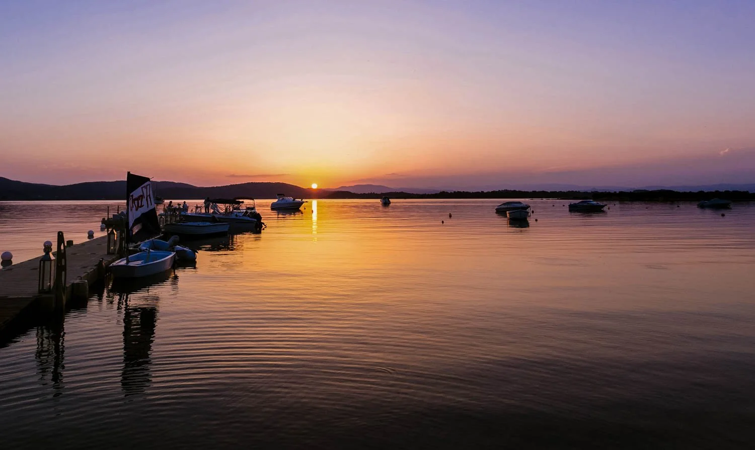 A sunset over a calm lake with boats docked at a wooden pier.