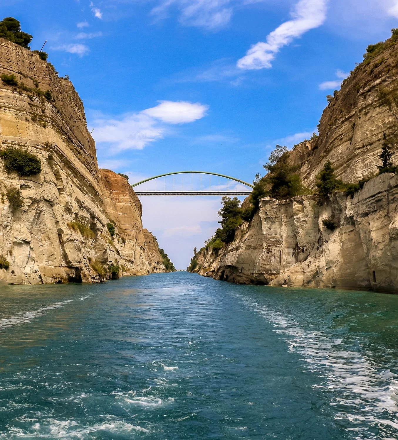 A view of a waterway with steep cliffs on both sides and a bridge in the distance under a blue sky with scattered clouds.