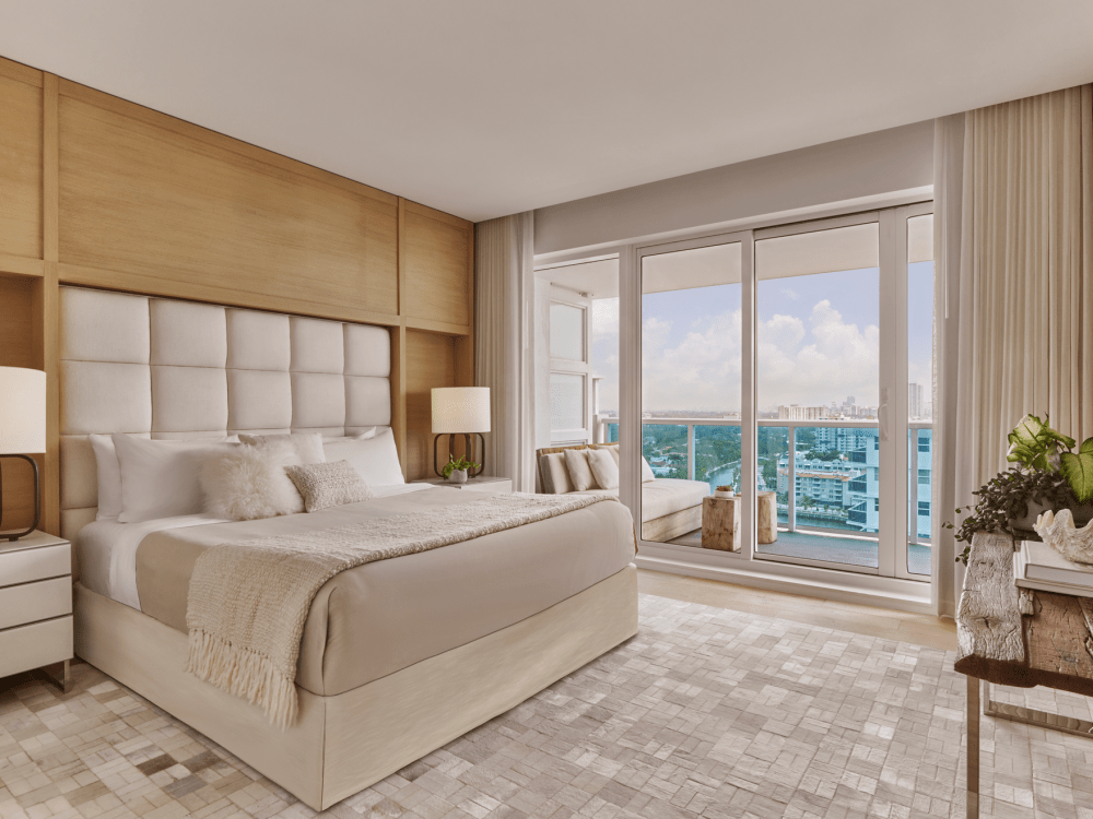 Luxury bedroom with large bed, wooden headboard, bedside tables with lamps, and sliding glass doors leading to a balcony with city view.