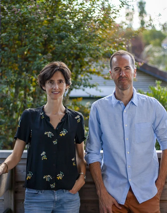 Duo de designers, Marion et Jullien Sauvée. Un homme et une femme debout sur un balcon en extérieur, avec des arbres en arrière-plan, dans une ambiance ensoleillée.