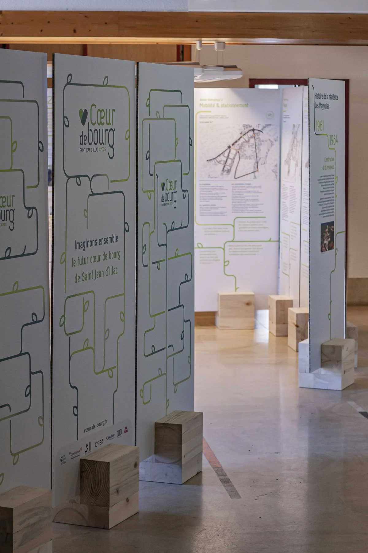 Scénographie d'exposition. Exposition avec de grands panneaux d'information insérés dans des piétements en bois clair.