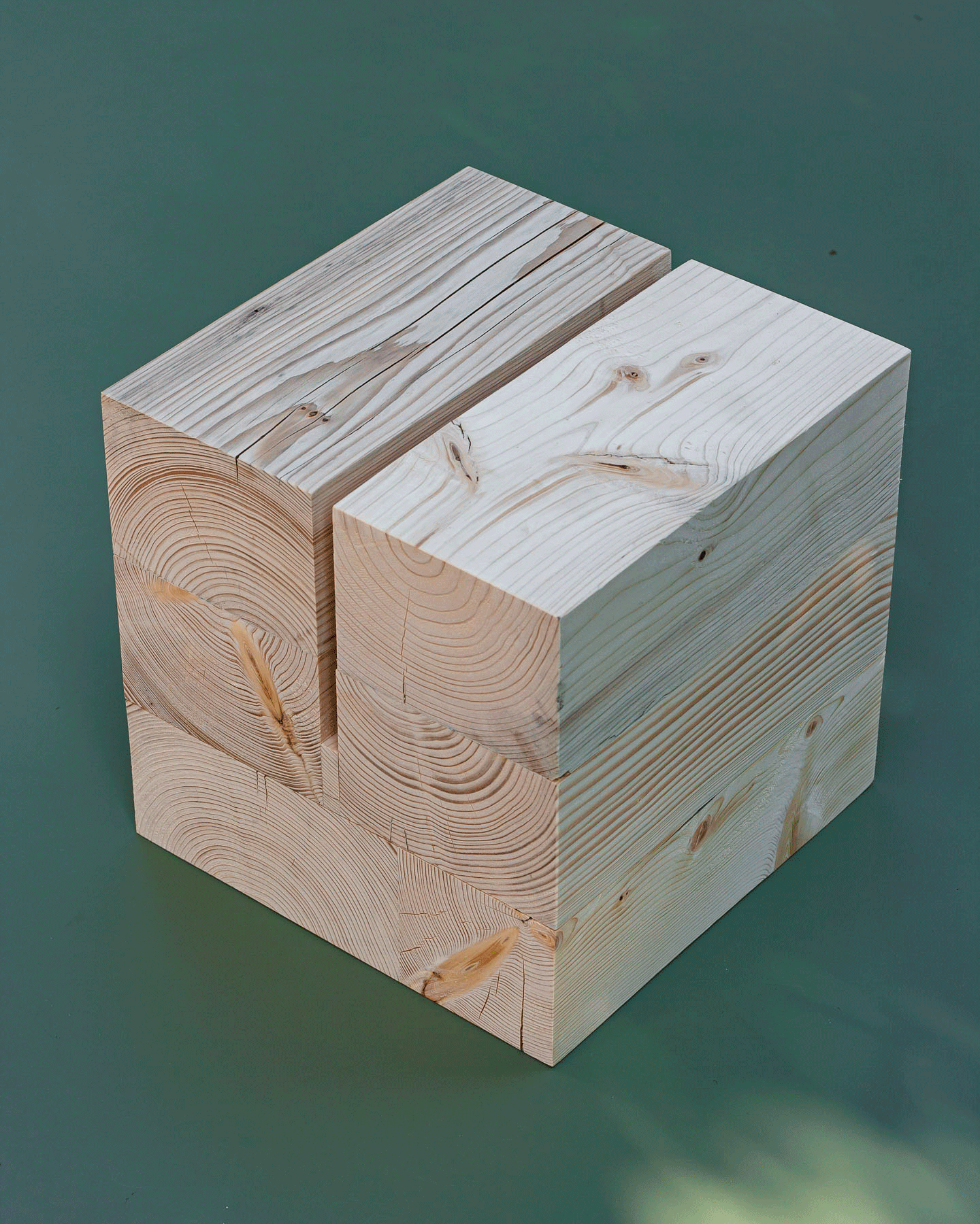 Scénographie d'exposition. Détail de la réalisation d'un piétement en bois de réemploi. Cube en bois clair pris en photo sur sur un fond vert.