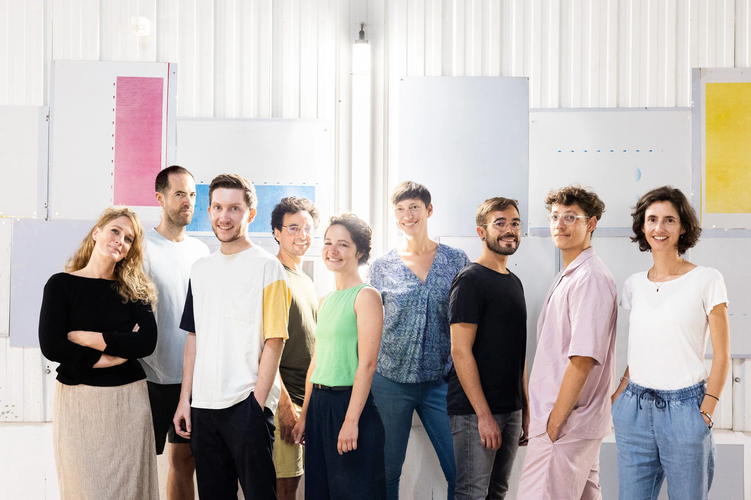Collectif de l'association Approche - Graphismes en Nouvelle Aquitaine. Groupe de personnes diverses posant ensemble dans une salle lumineuse avec des panneaux colorés en arrière-plan.