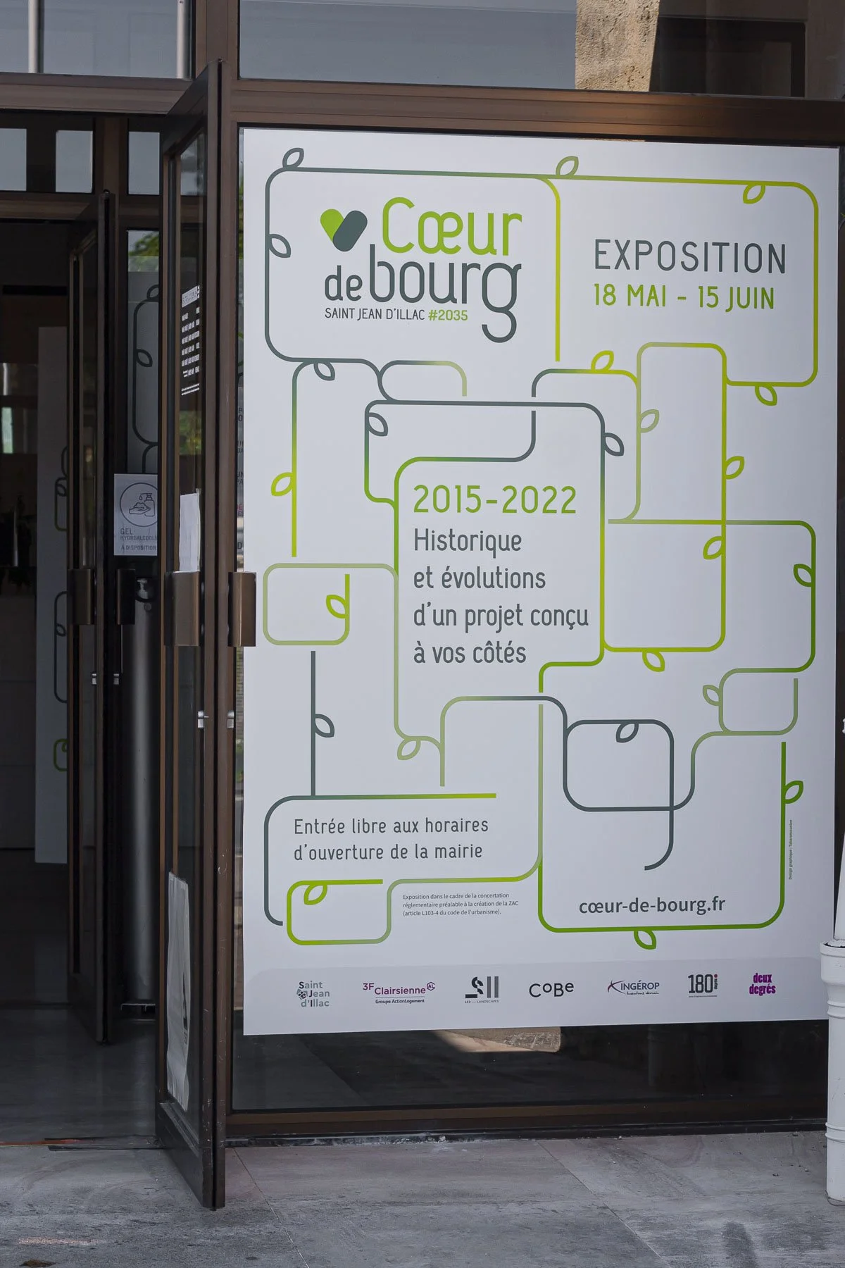Une affiche annonçant une exposition intitulée "Cœur de Bourg" à Saint Jean d'Illac, du 18 mai au 15 juin, avec une histoire de 2015 à 2022 et indiquant une entrée libre pendant les heures d'ouverture de la mairie.