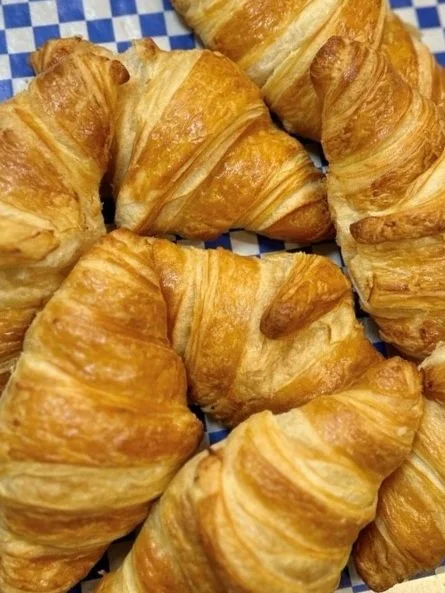 Close-up of several golden-brown croissants on a blue and white checkered surface.