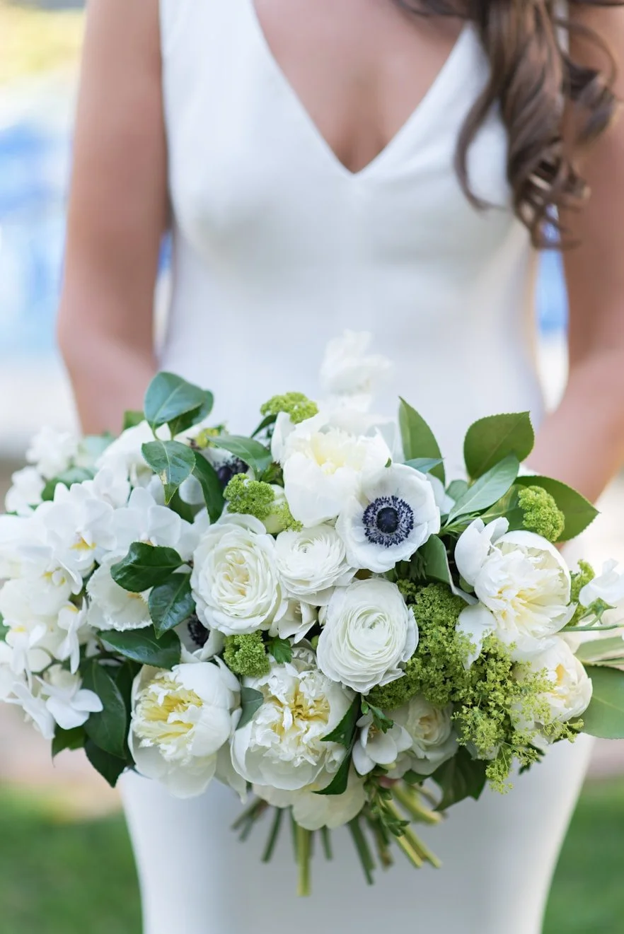A woman in a white dress holding a bouquet of white and green flowers.