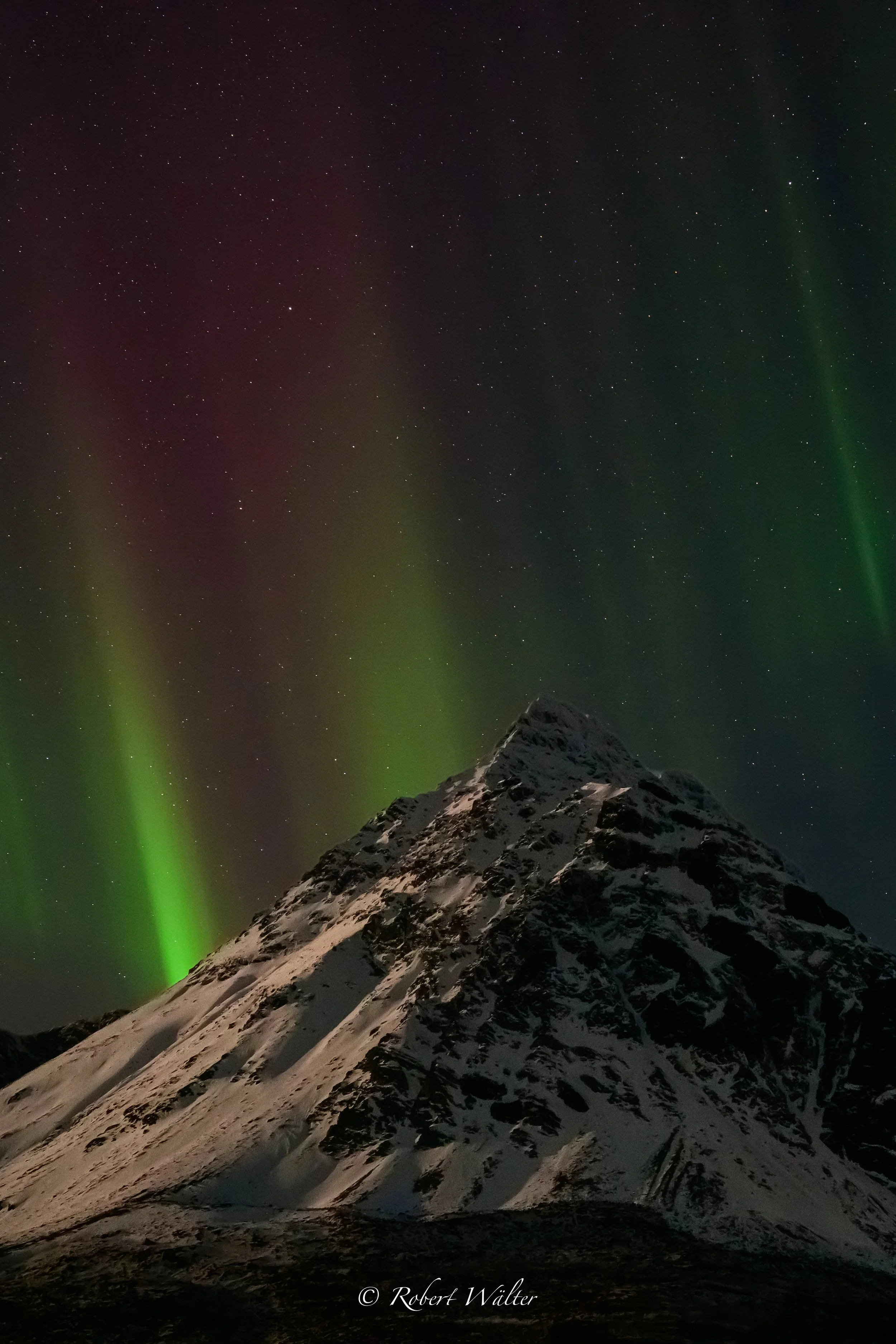 Schneebedeckter Berg unter Nordlichtern und Sternenhimmel in der Nacht, fotografiert von Robert Wälter.