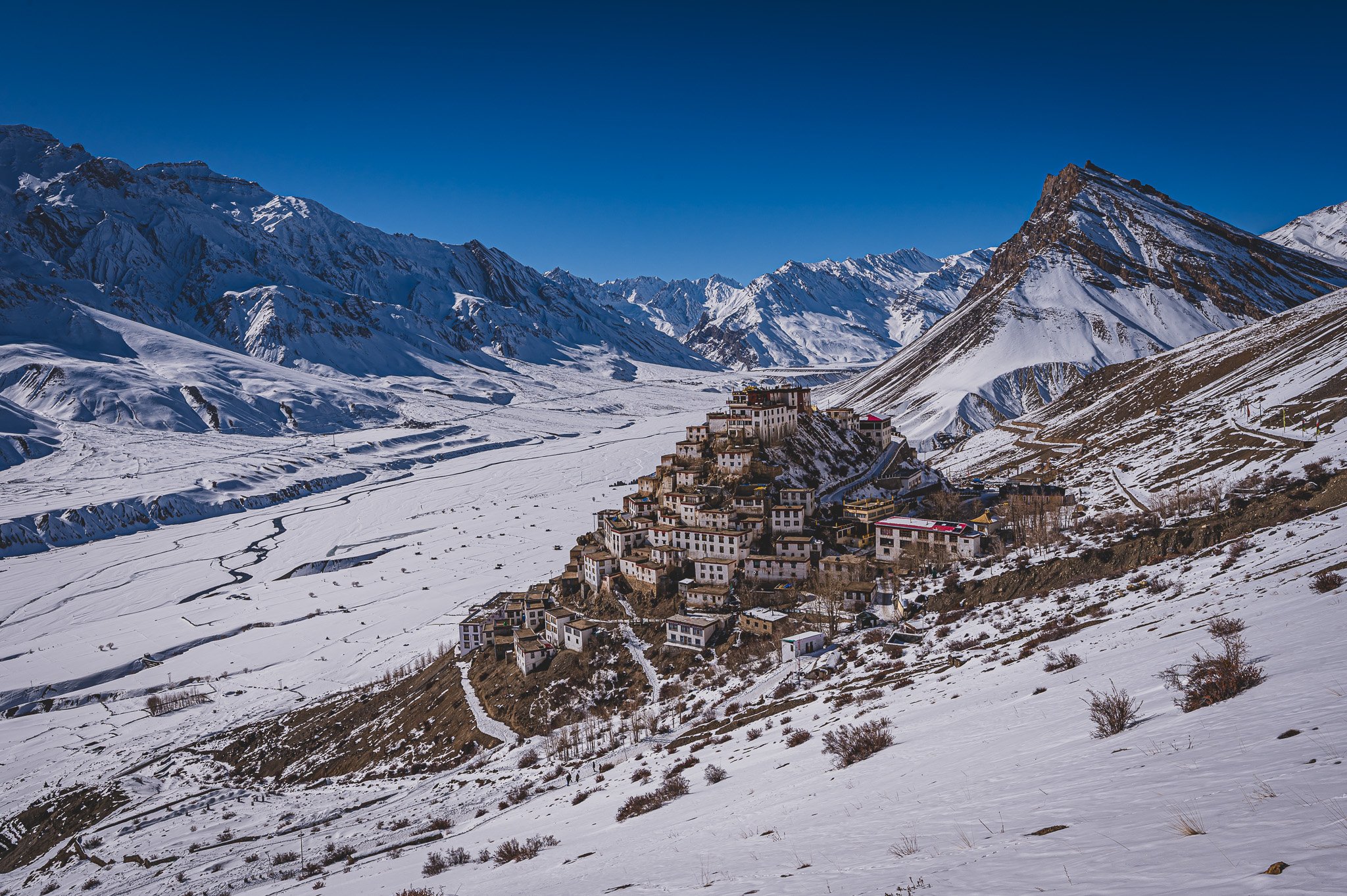Ein verschneites Bergdorf am Hang mit weißen Gebäuden und schneebedeckten Bergen im Hintergrund.