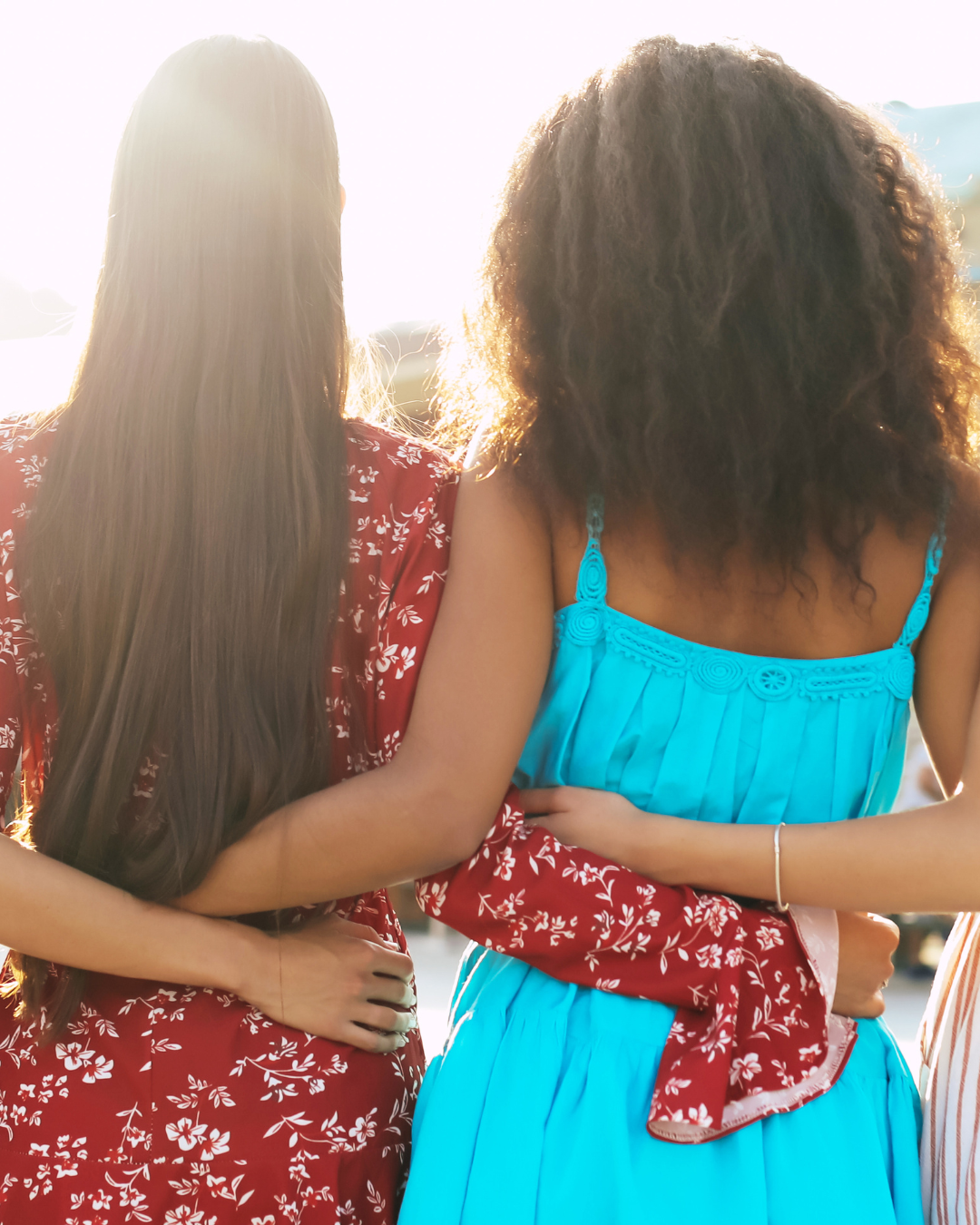 two women linking arms together, facing the sun