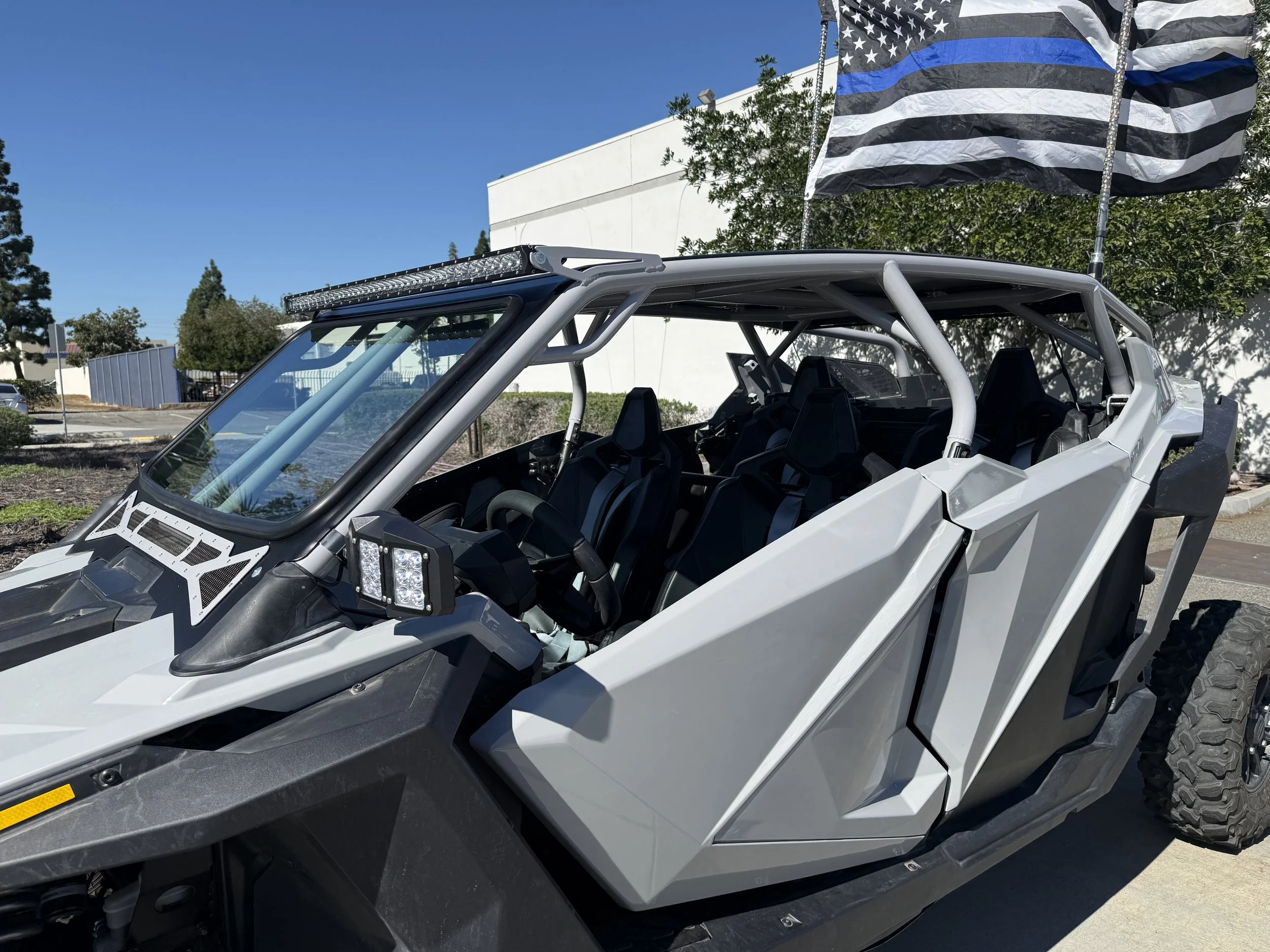 A side view of a futuristic off-road vehicle with a white and black exterior, open cabin, and flag with a black and white striped pattern flying behind it in a parking lot.