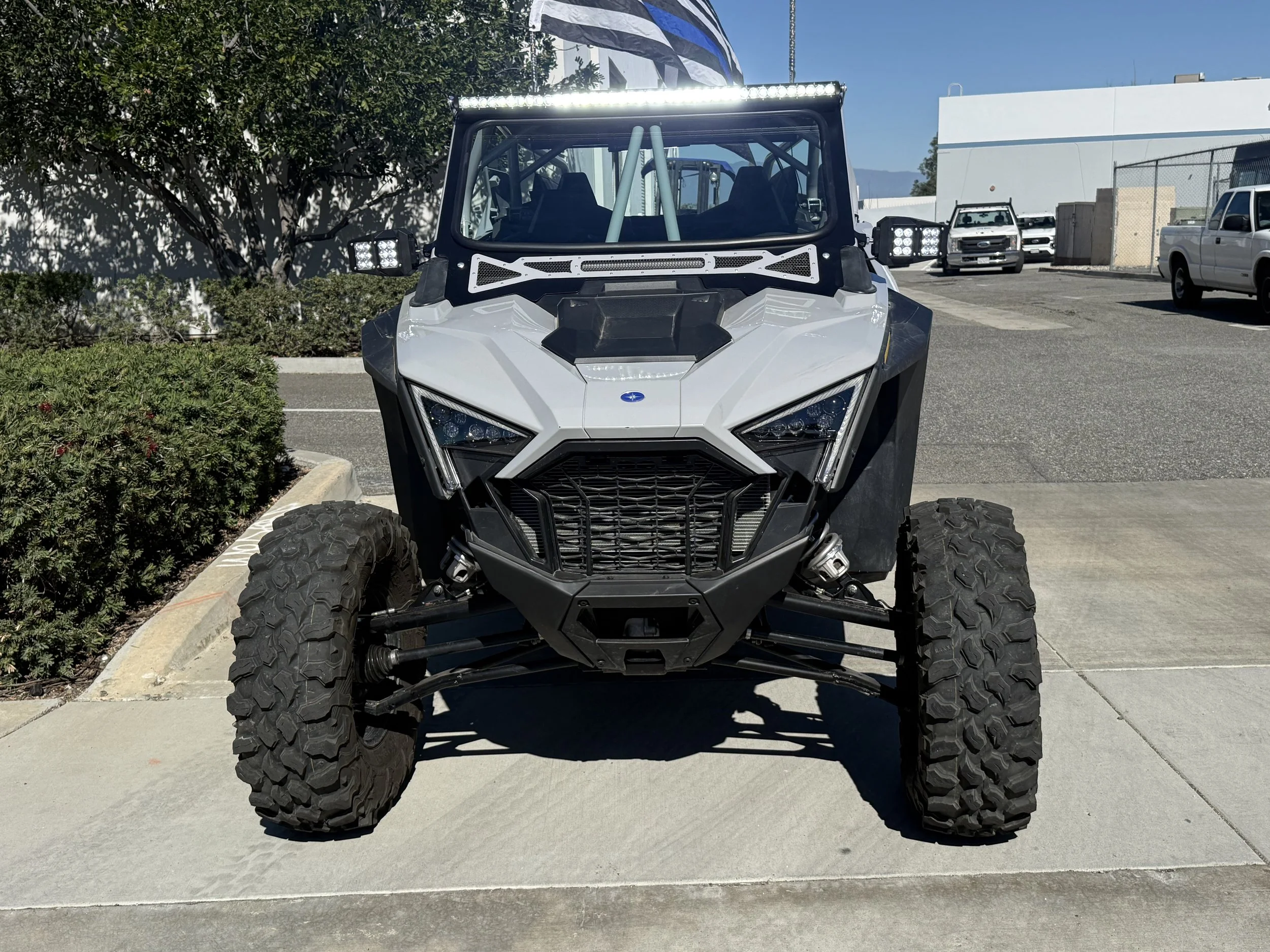 Front view of a white off-road utility vehicle with large tires, parked on a concrete sidewalk in a parking lot.