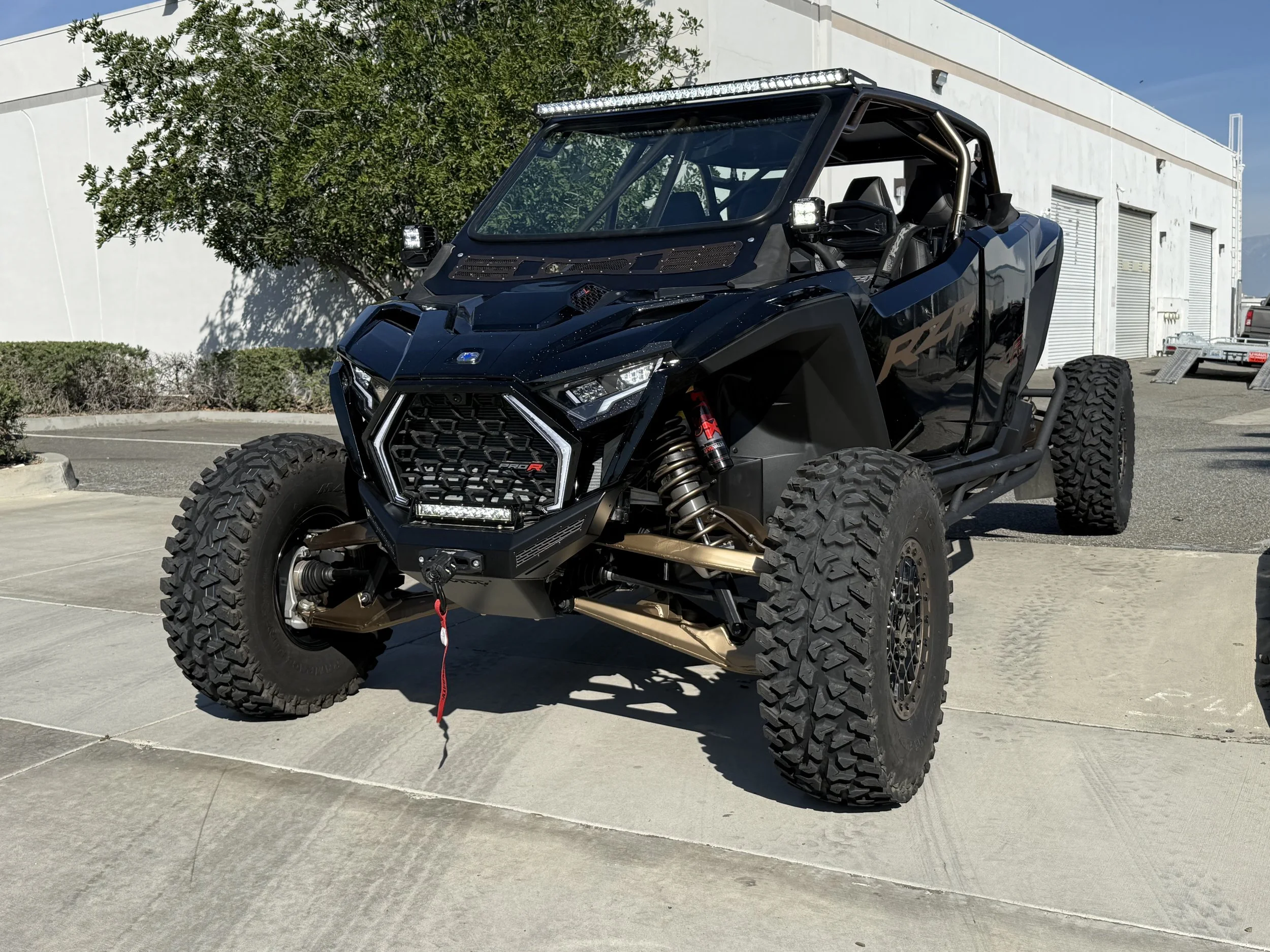 Black off-road utility terrain vehicle with large tires, suspension, and roll cage parked on concrete pavement outside a building.