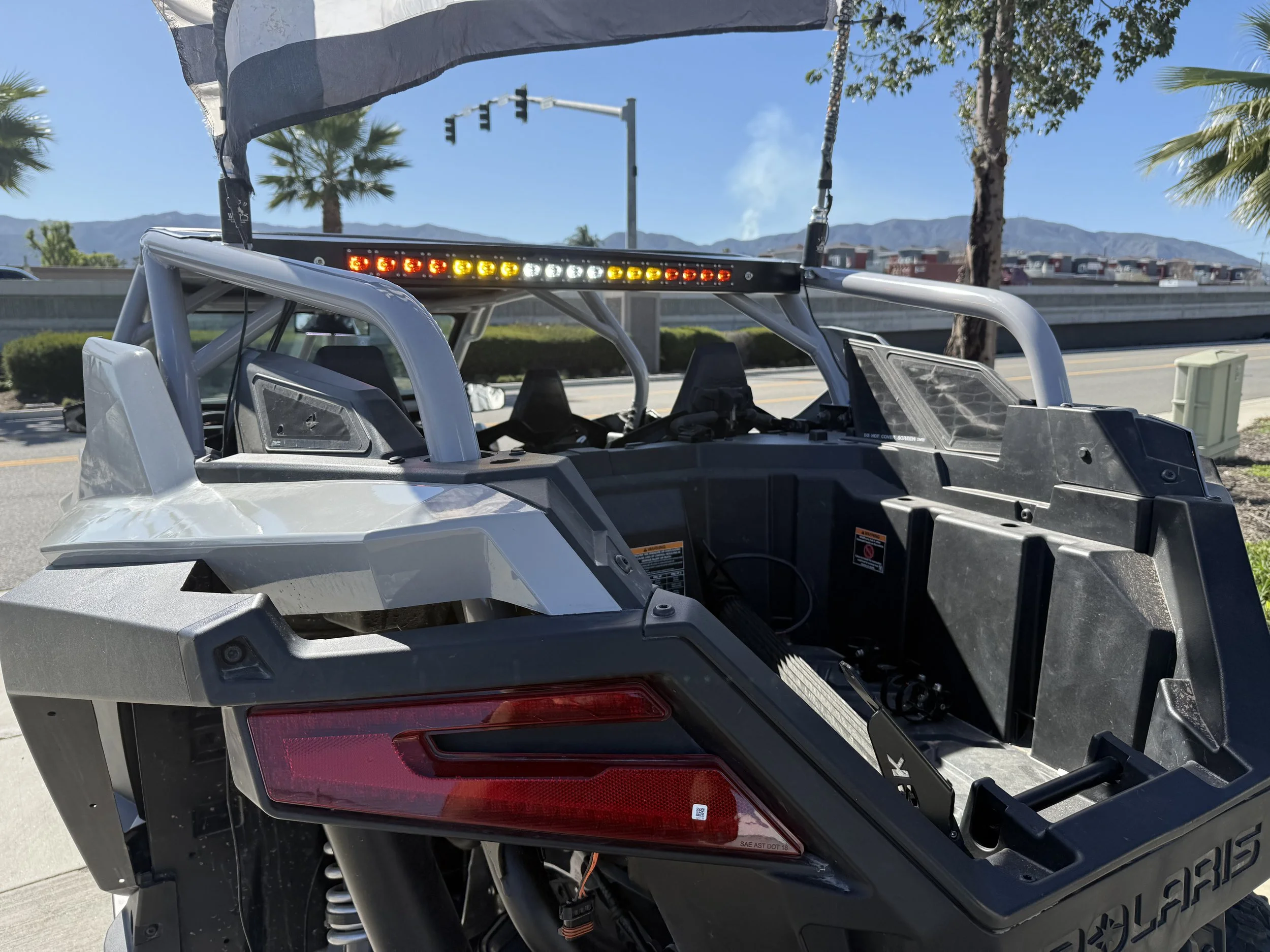 Empty Polaris off-road vehicle with flashing emergency lights and a canopy, parked near trees and mountains in the background.