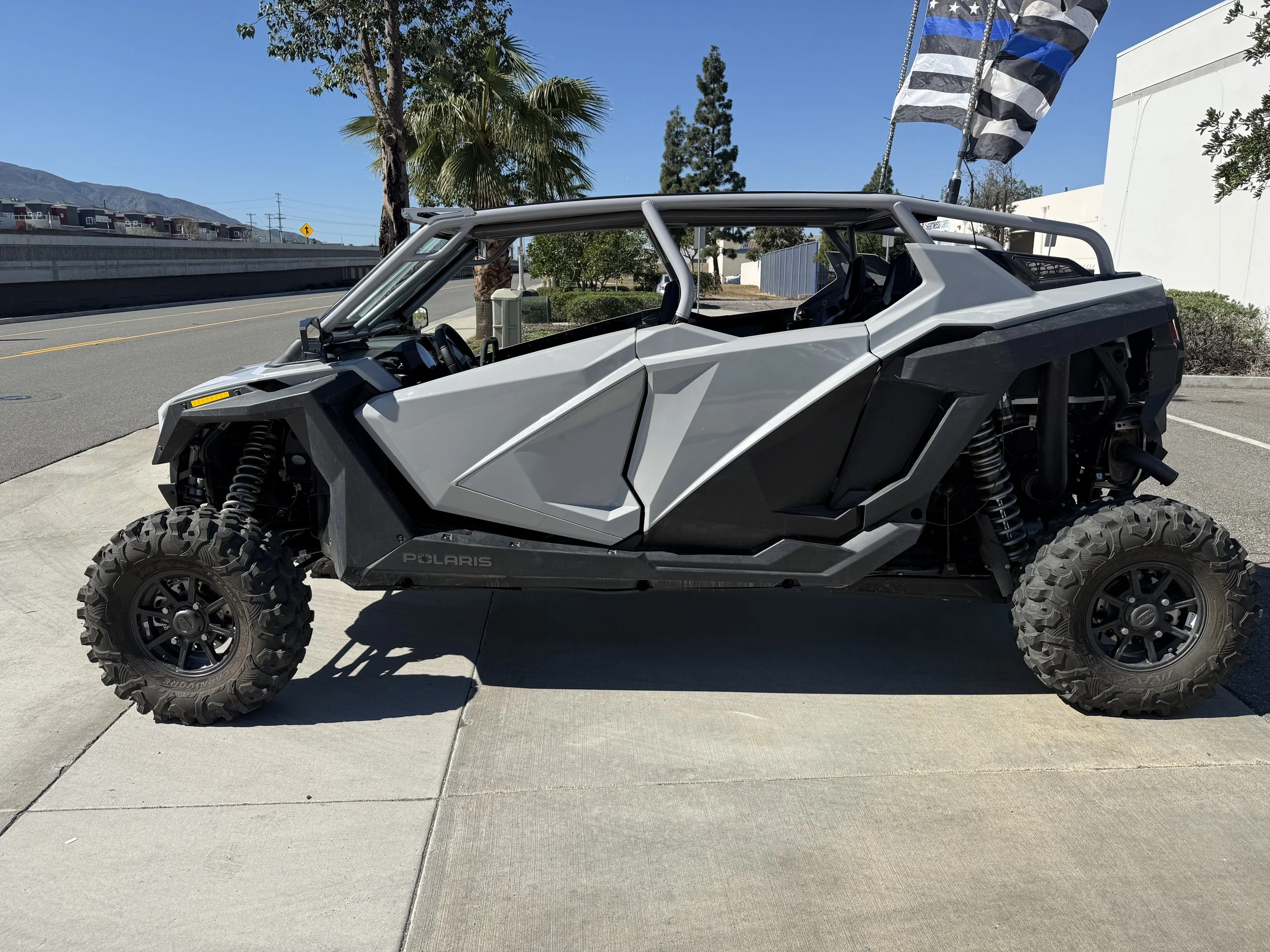Gray off-road Polaris side-by-side vehicle parked on a sidewalk with flags flying behind it.