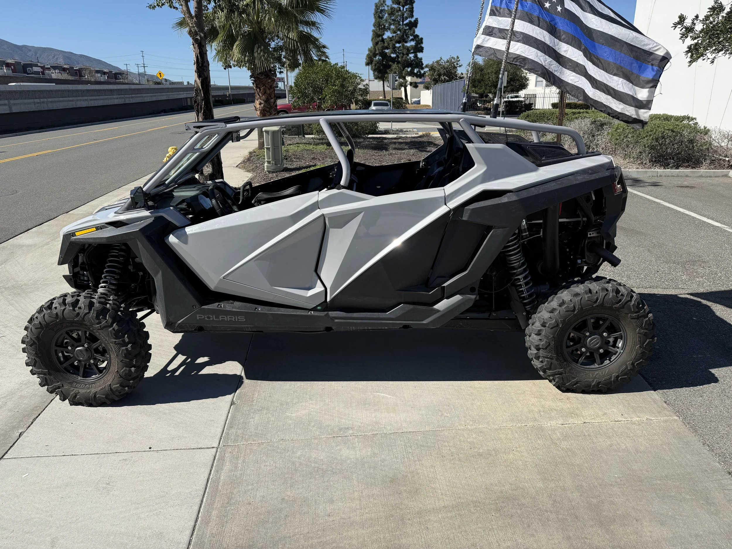 A gray Polaris off-road utility vehicle parked on a concrete sidewalk, with black tires, open cabin, and a Kansas City police flag flying nearby.