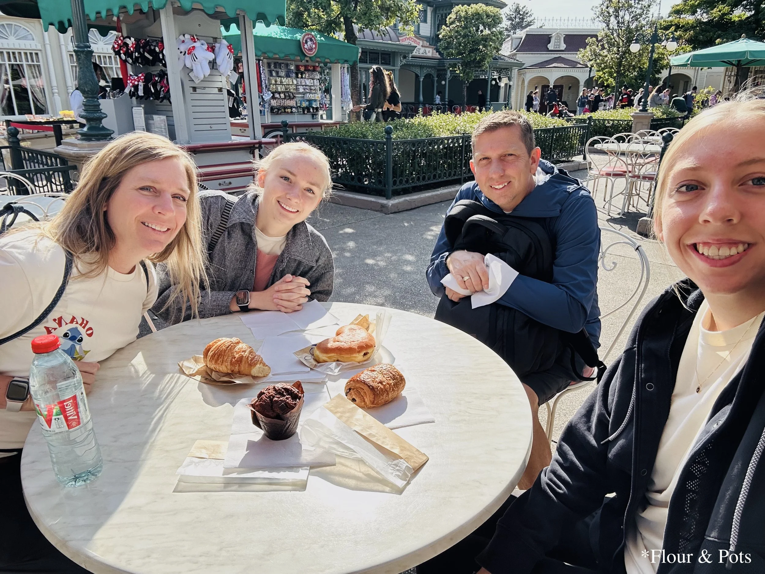 Family enjoying a quick breakfast of pastries and muffins on Main Street, with Sleeping Beauty’s Castle in Disneyland Paris near by.