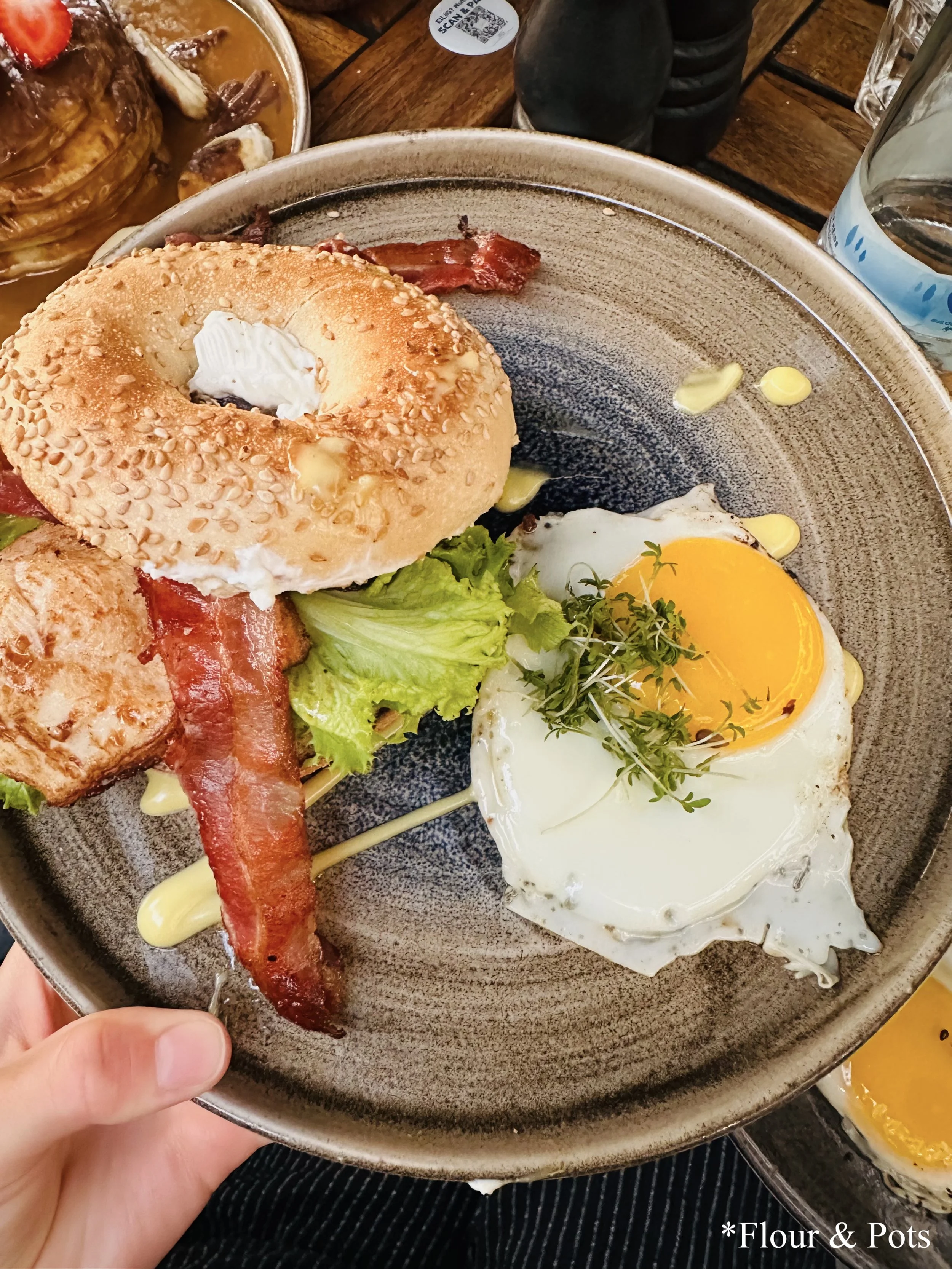 Chicken BLT bagel from Cotidiano in Munich, Germany, featuring a sesame bagel filled with chicken breast, cream cheese, bacon, lettuce, tomato, and a fried egg.