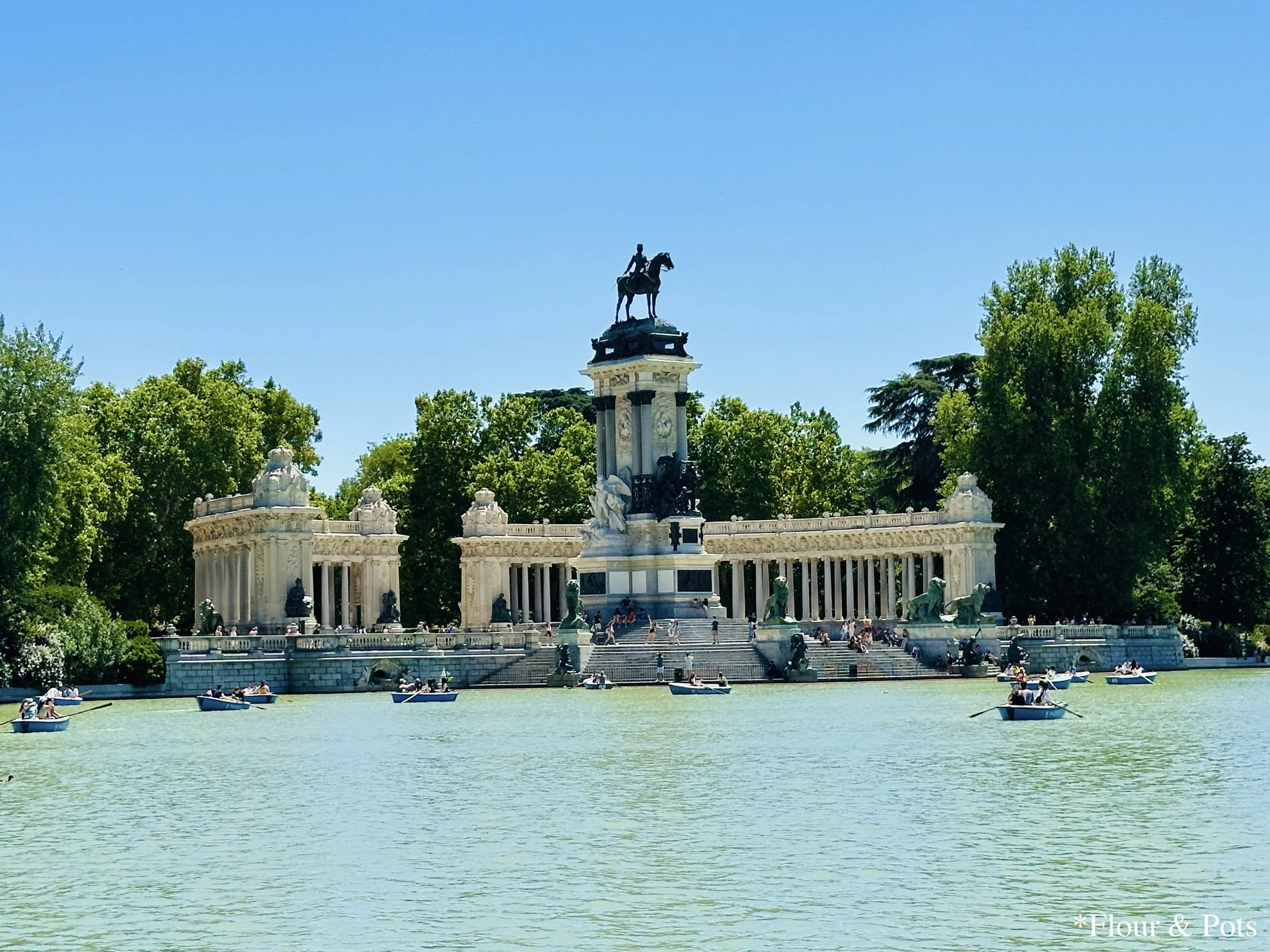 The Estanque Grande del Retiro in Madrid’s Retiro Park, with people paddling boats on the serene waters under the sunny sky.
