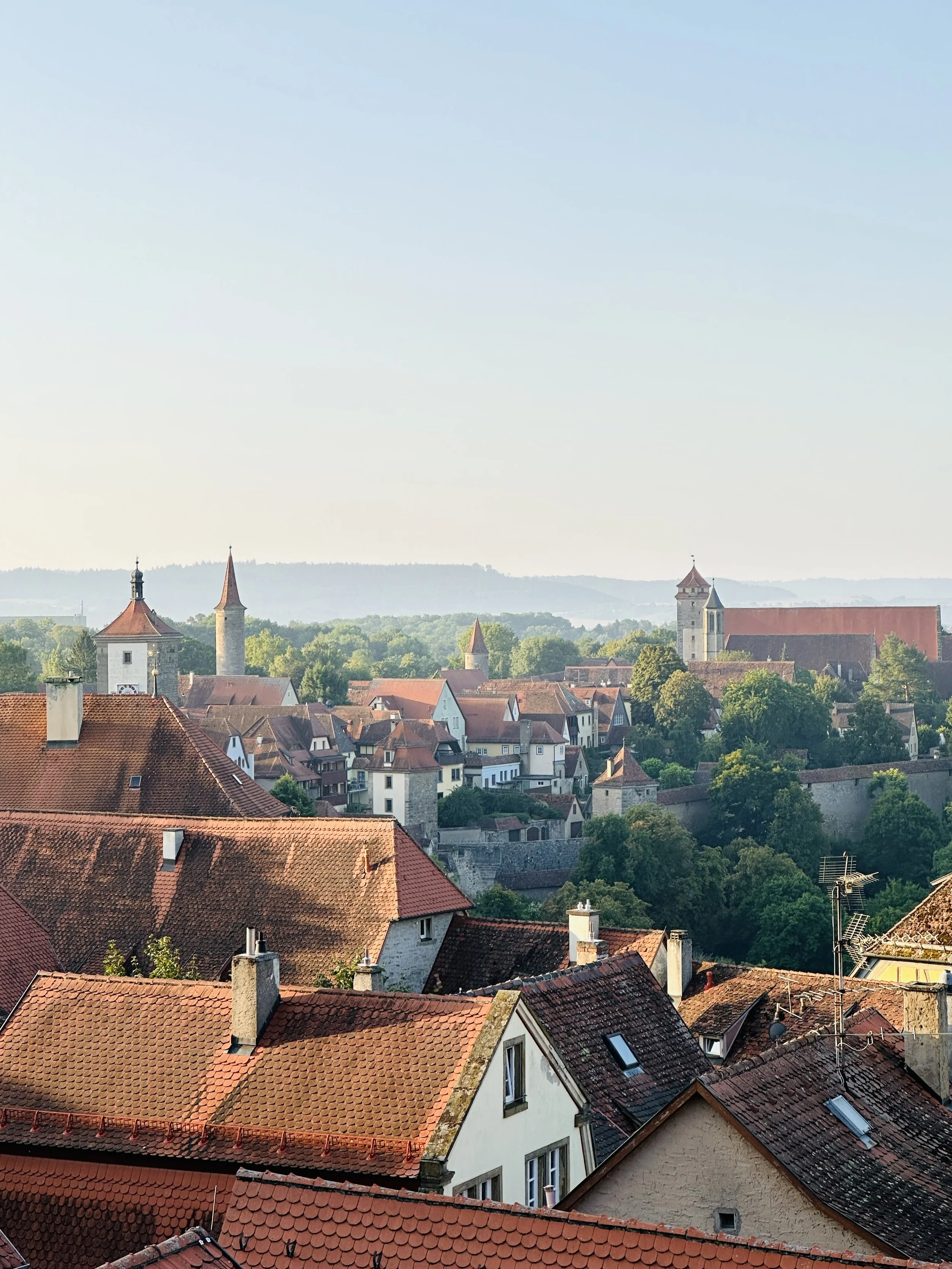 Panoramic view of Rothenburg ob der Tauber, Germany, from a deck, showcasing the medieval town's rooftops, city walls, and surrounding greenery.