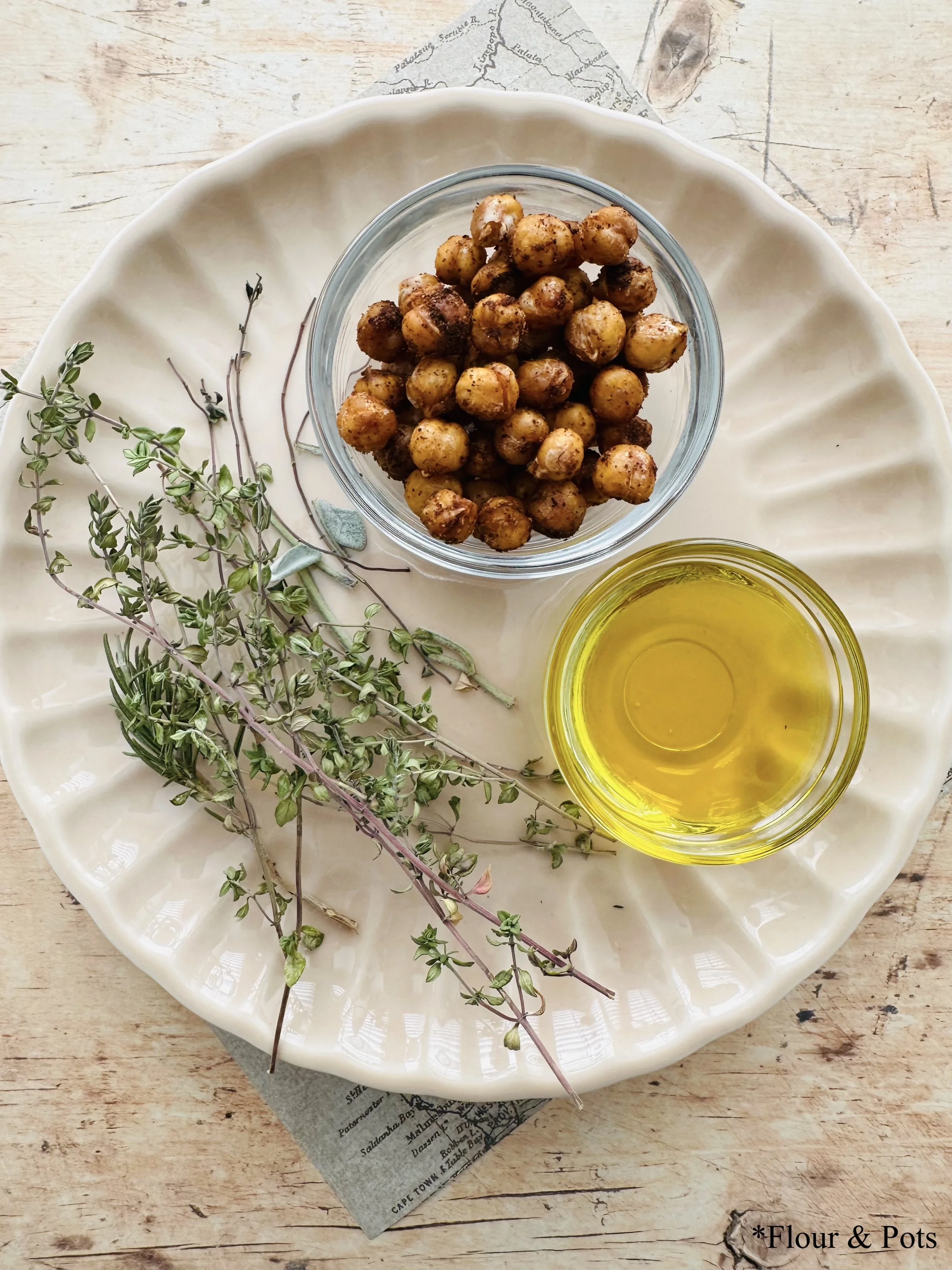 A plate showcasing fresh herbs, olive oil, and roasted seasoned chickpeas, highlighting the natural ingredients used to make the creamy hummus.