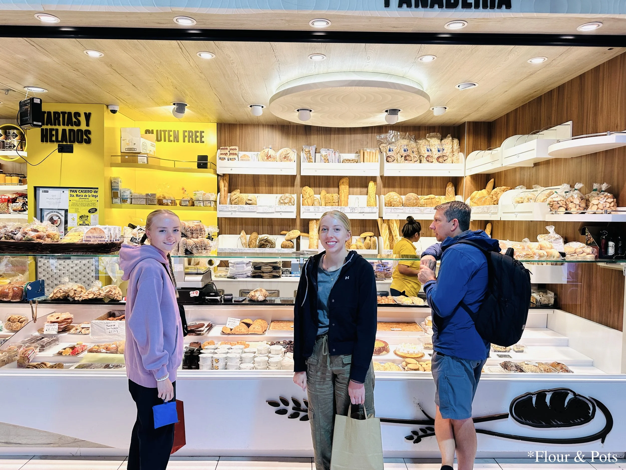 A scene at Mercado de la Paz in Madrid, Spain, where a family is purchasing fresh bread at a bright market stall.