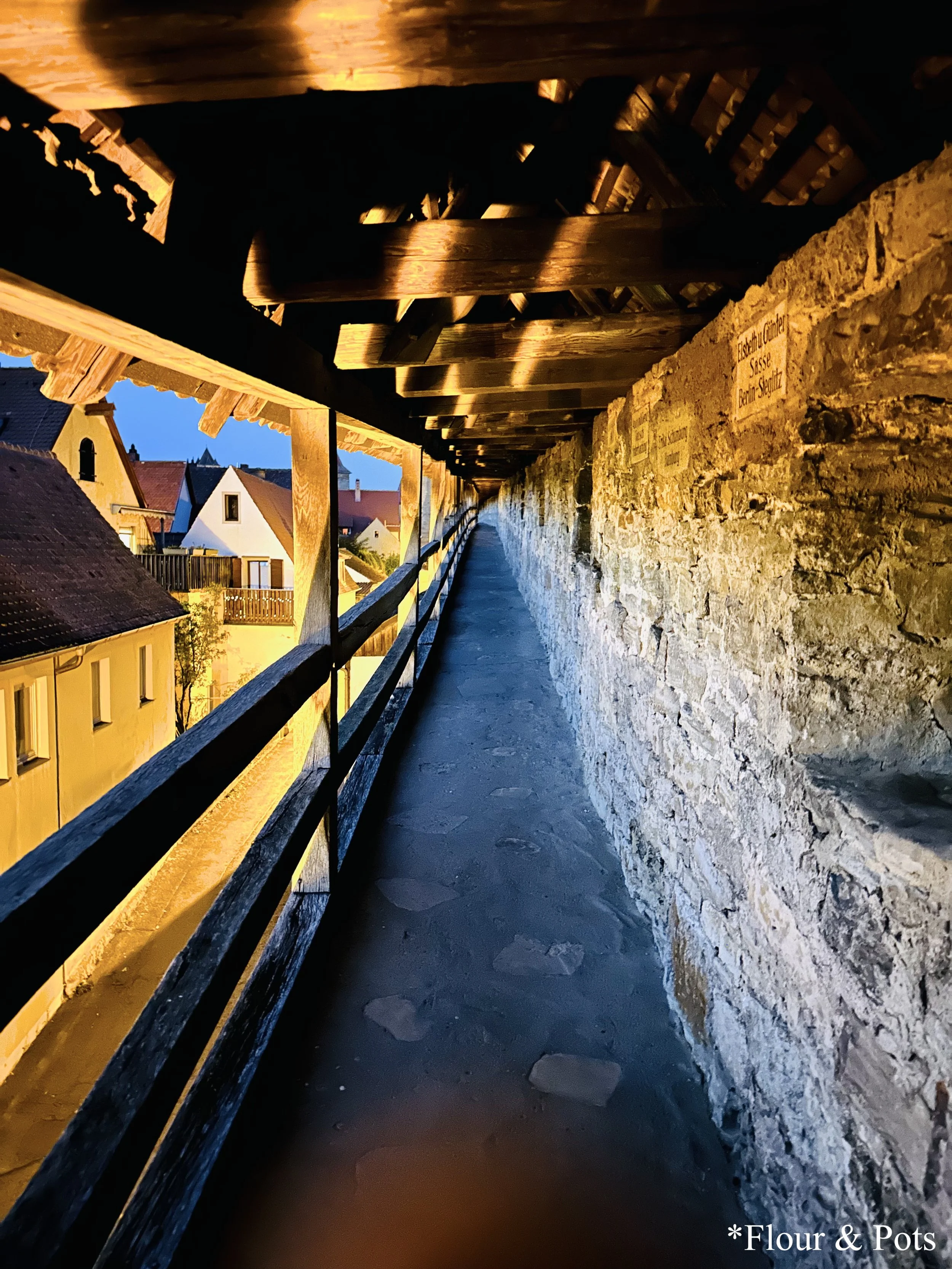 Nighttime view of the city wall in Rothenburg, Germany, with illuminated pathways and a glimpse of the medieval architecture.