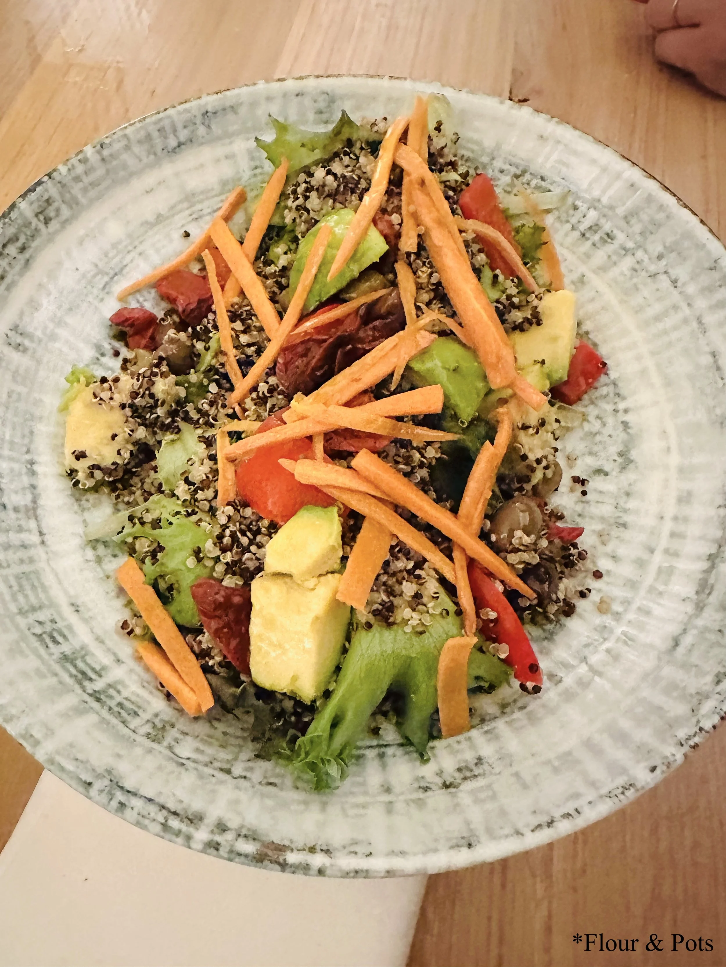 Colorful quinoa salad from Obicá in Rome, Italy, featuring creamy avocado chunks, shredded carrots, red peppers, and a light olive oil and vinegar dressing.