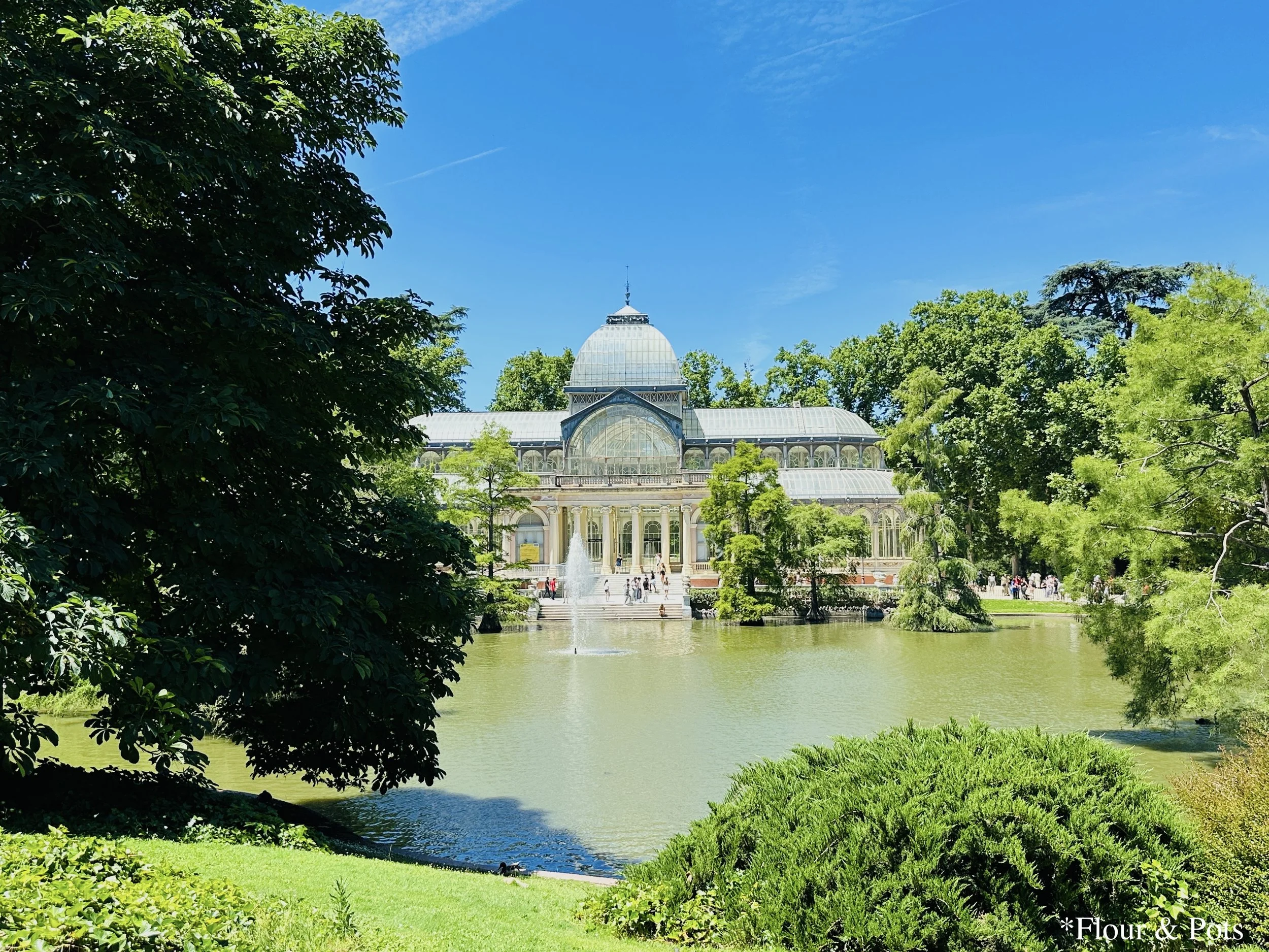 The Crystal Palace in Retiro Park, Madrid, showcasing its glass and iron architecture against a clear blue sky.