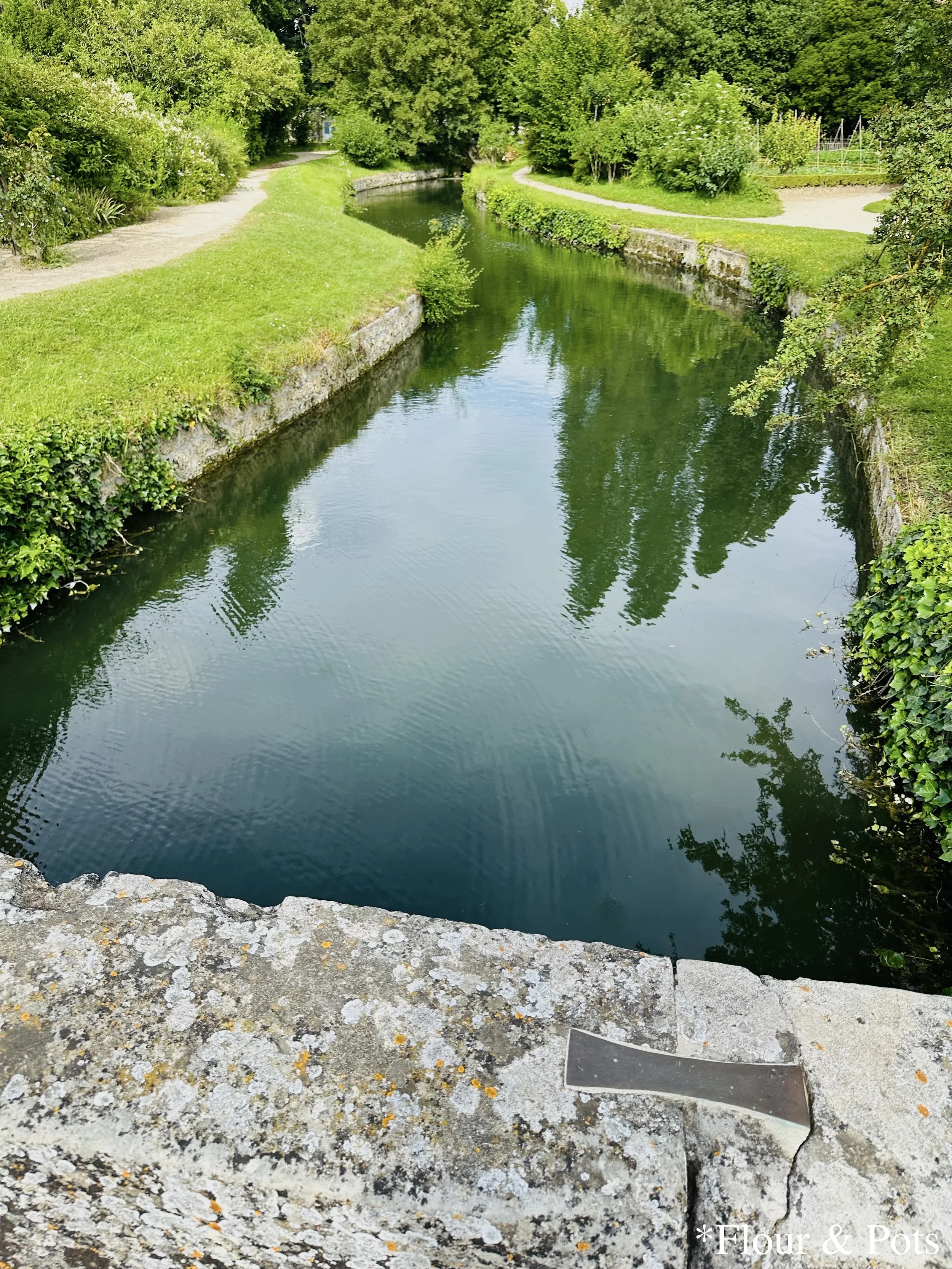A winding river flowing under a stone bridge at the Queen’s Hamlet, Palace of Versailles.