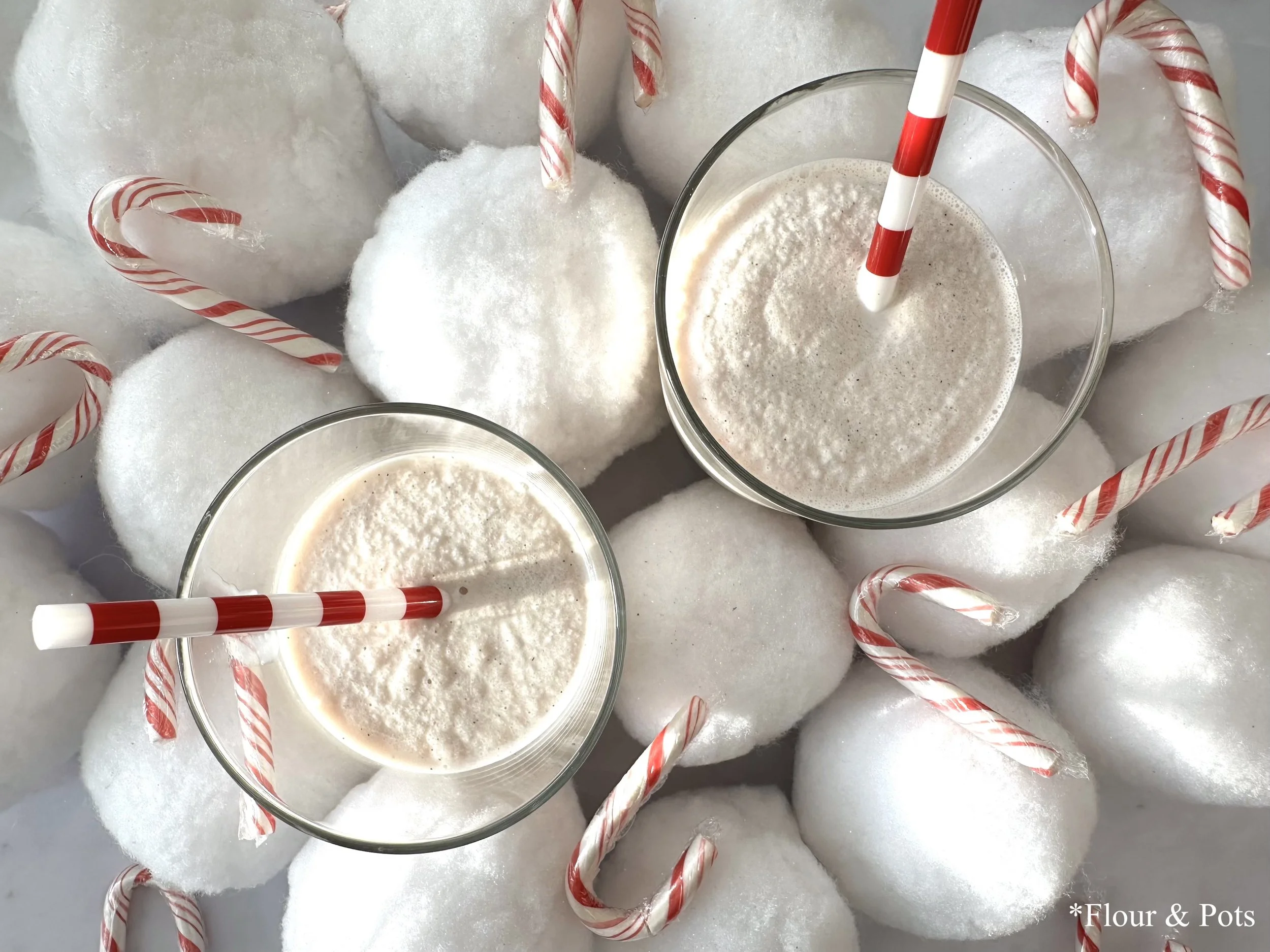 Two tall glasses filled with creamy peppermint candy cane smoothies, topped with crushed candy canes and a festive garnish, sitting on a light background.