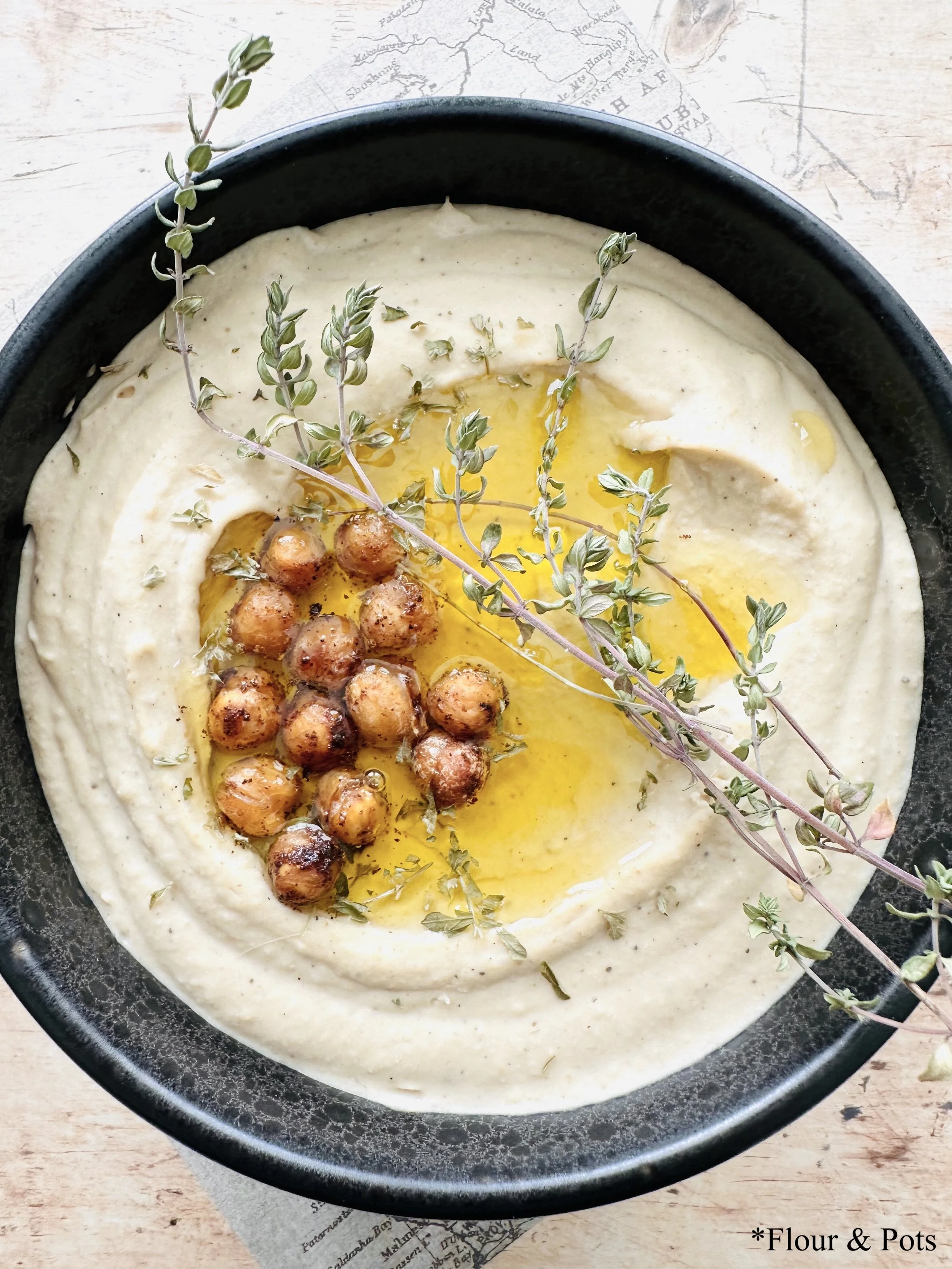Close-up of creamy hummus topped with a drizzle of olive oil, fresh herbs, and roasted, seasoned chickpeas, showcasing its smooth texture and vibrant garnishes.