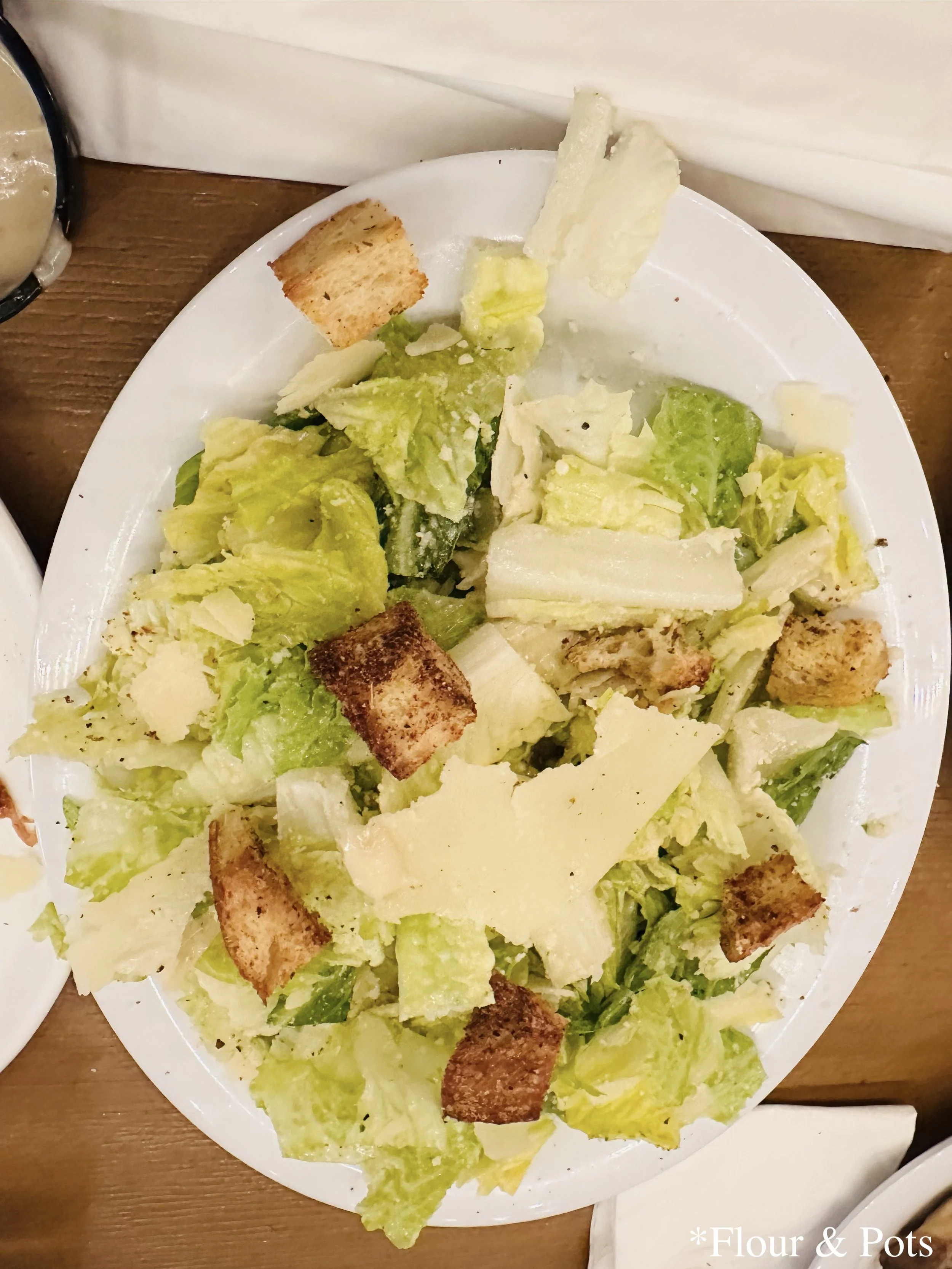 A freshly prepared Caesar salad from Red Oven Pizza at Universal Orlando CityWalk in Orlando, Florida, featuring crisp romaine lettuce, shaved Parmesan, croutons, and Caesar dressing, served in a white bowl.