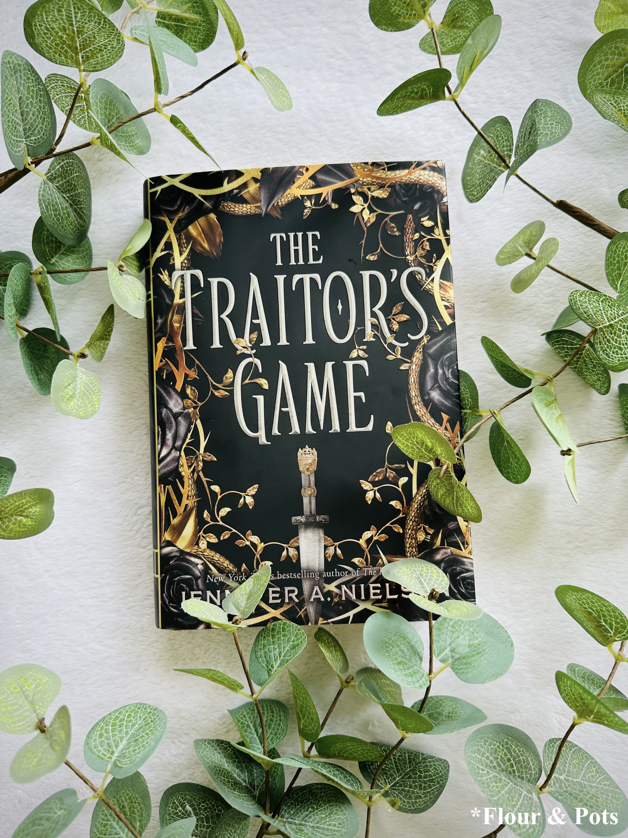 YA fantasy novel The Traitor’s Game styled in a moody setup highlighting themes of war, loyalty, and hidden identity