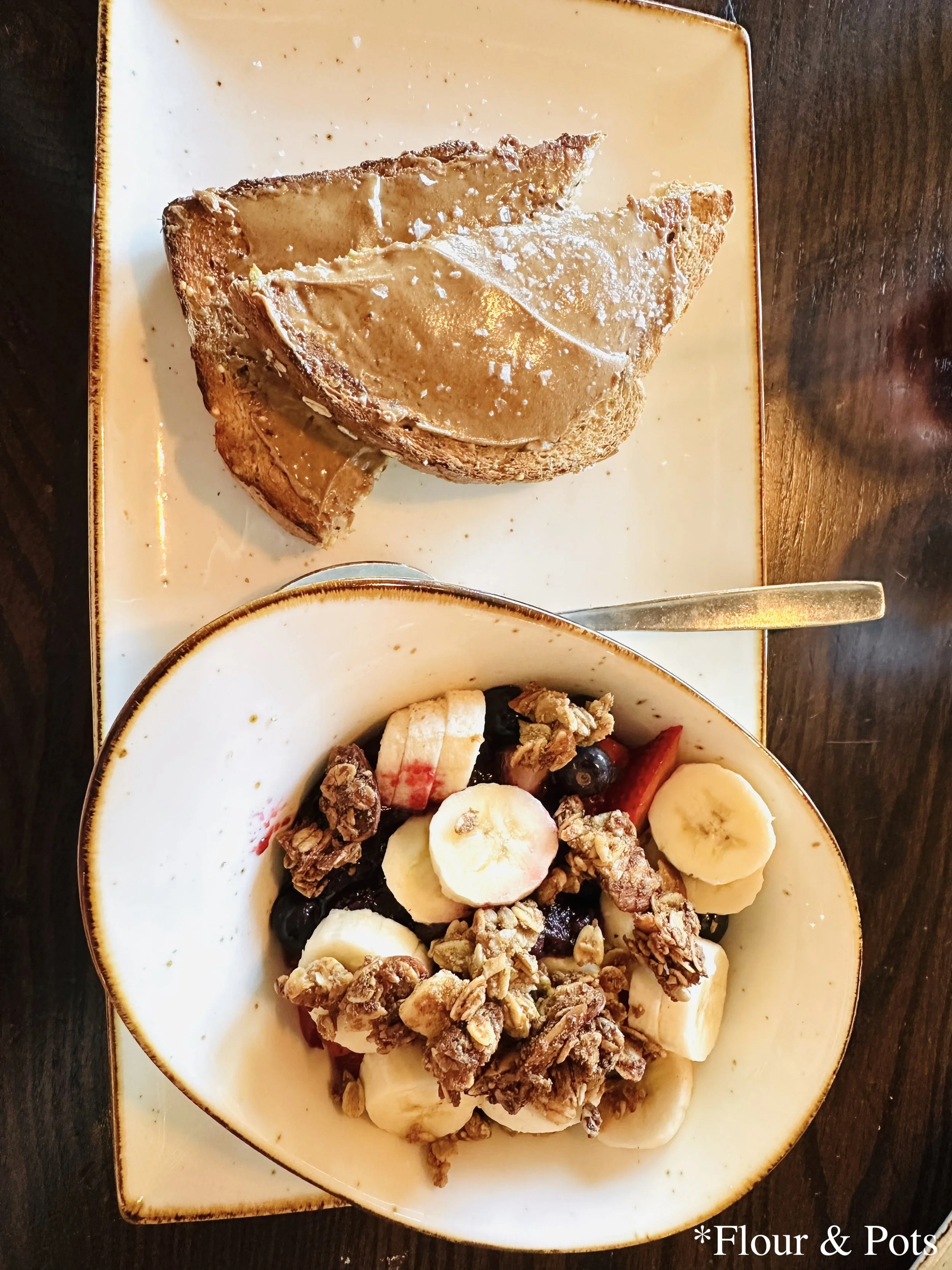 First Watch's A.M. Superfoods Bowl, featuring a colorful mix of fresh fruit, coconut, and chia pudding, served alongside toasted whole grain bread with a generous spread of almond butter.