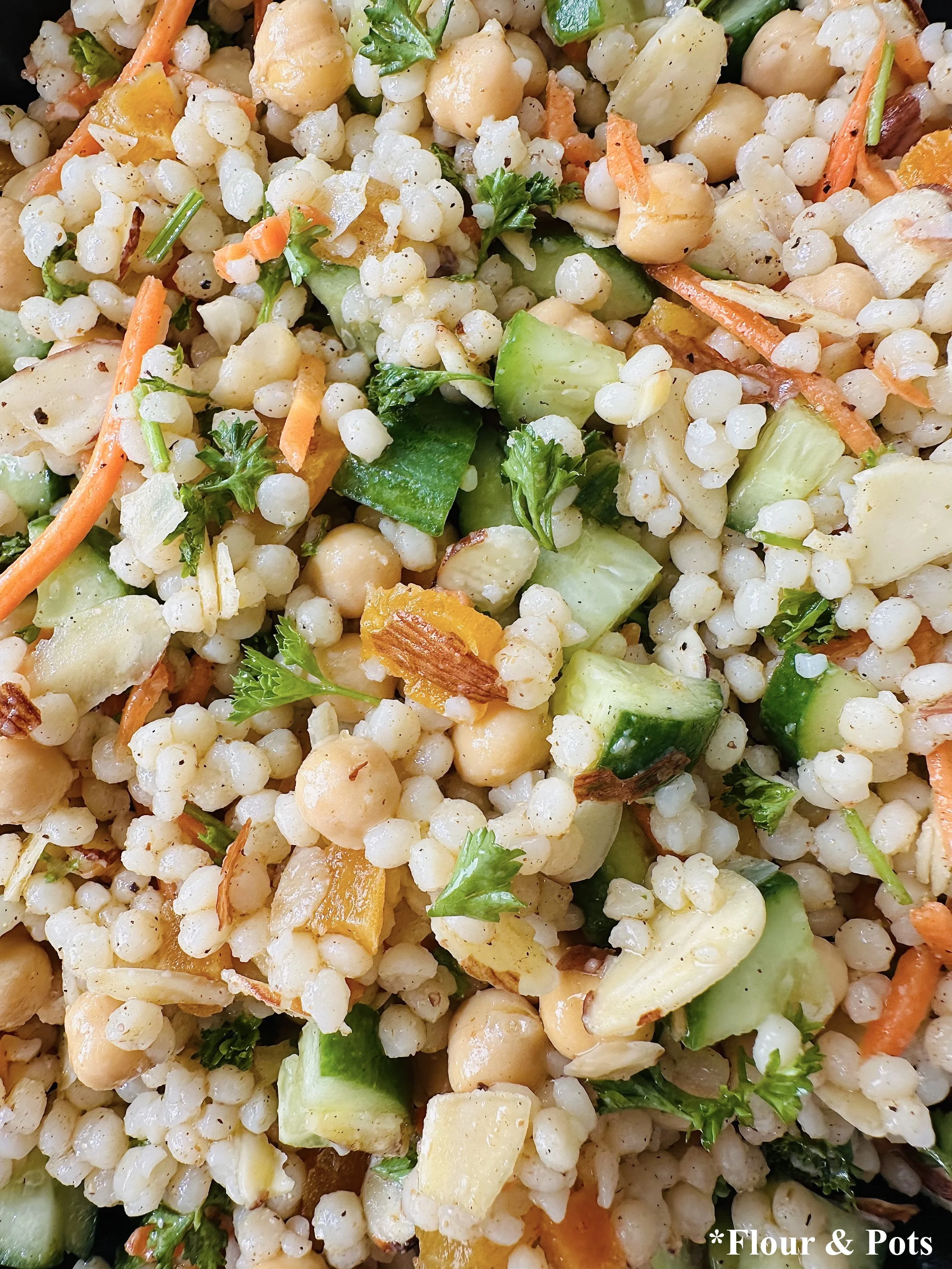 Close-up of colorful couscous salad showing pearl couscous, shredded carrots, parsley, and sliced almonds