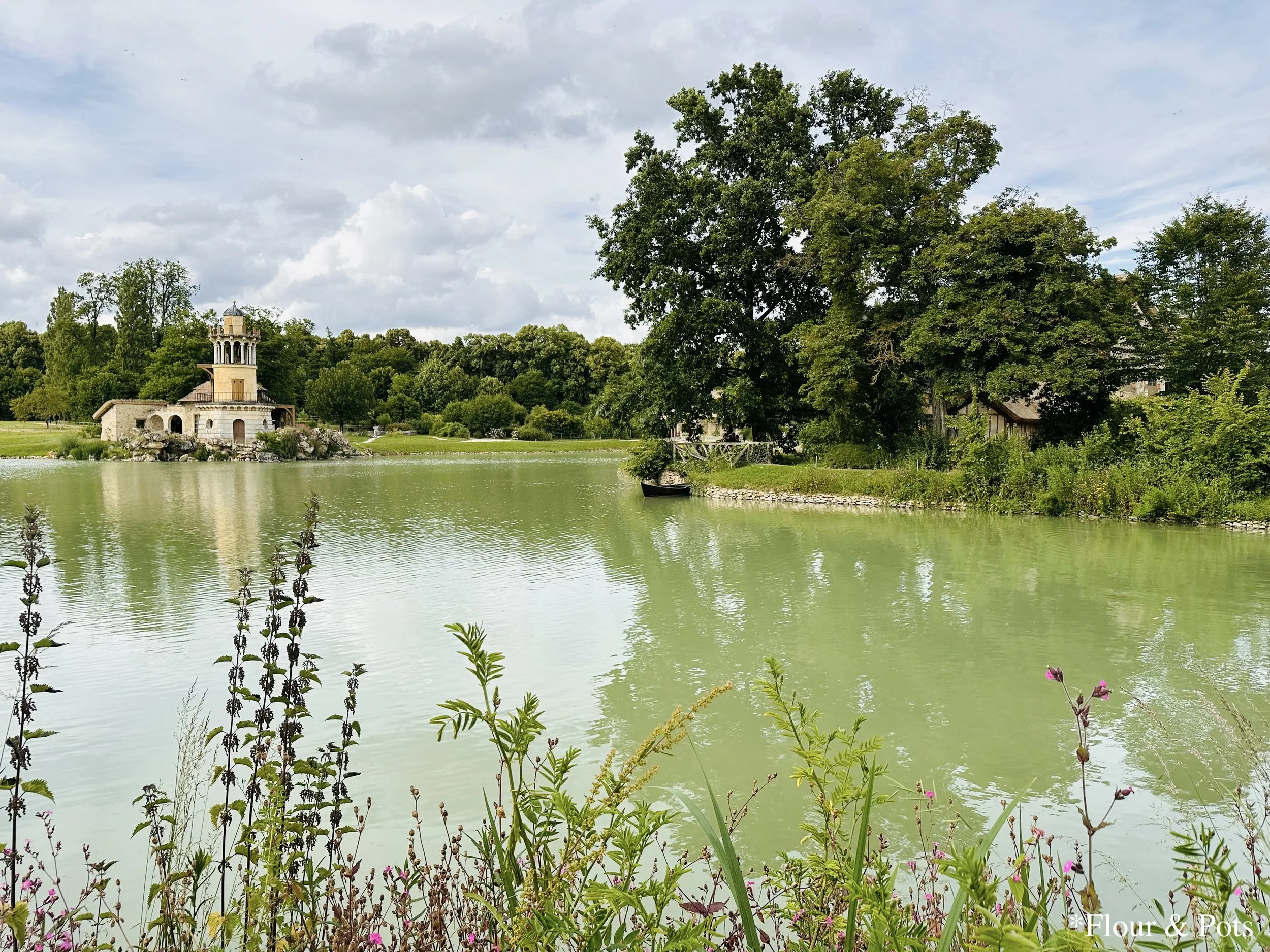 Scenic view of the peaceful lake surrounded by rustic cottages and greenery at the Queen’s Hamlet, Palace of Versailles, Paris, France.