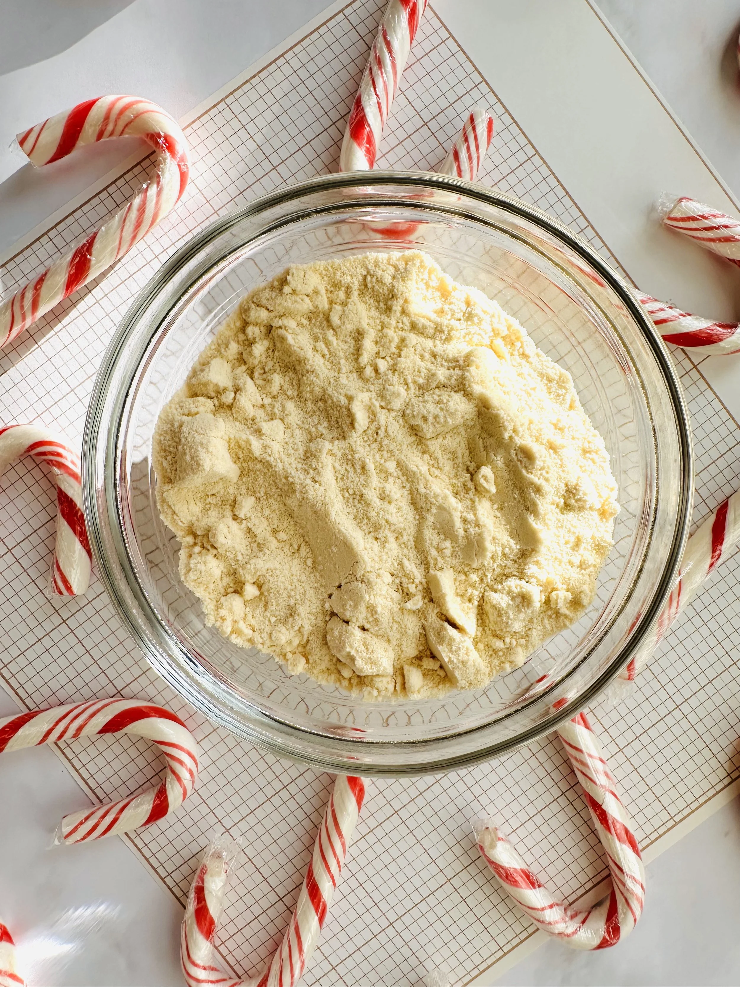 A small bowl of malted milk powder with red and white candy canes blurred in the background.